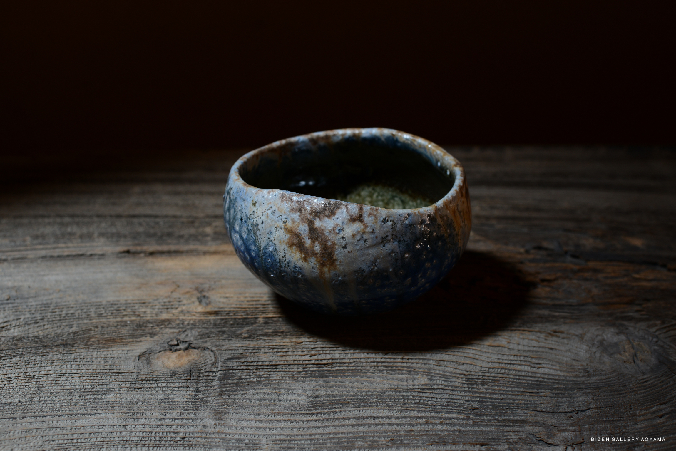 A handcrafted blue and brown ceramic bowl placed on a wooden surface, showcasing its unique texture and form.