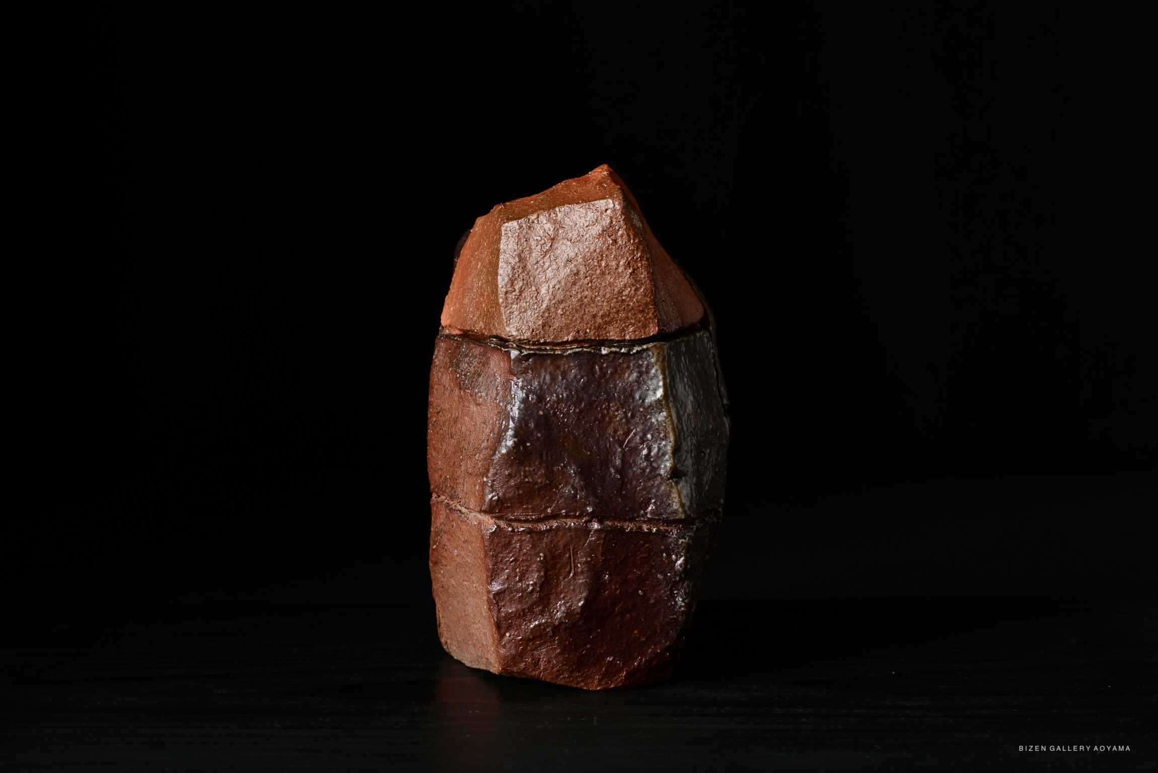 A unique, angular ceramic piece designed with a blend of earthy browns and textures, set against a black background.