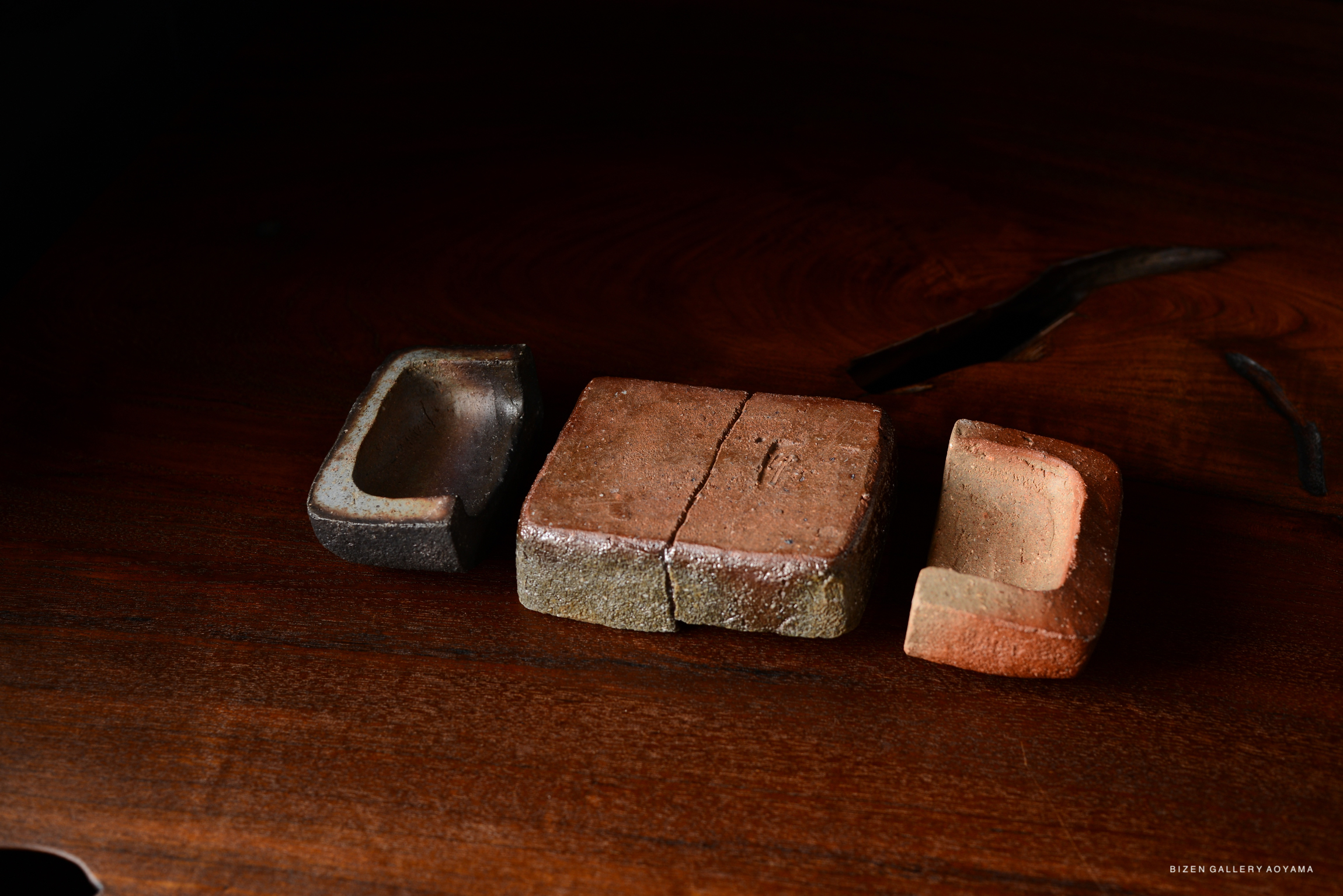 Three unique Bizen pottery pieces displayed on a wooden surface, showcasing their distinct shapes and colors.
