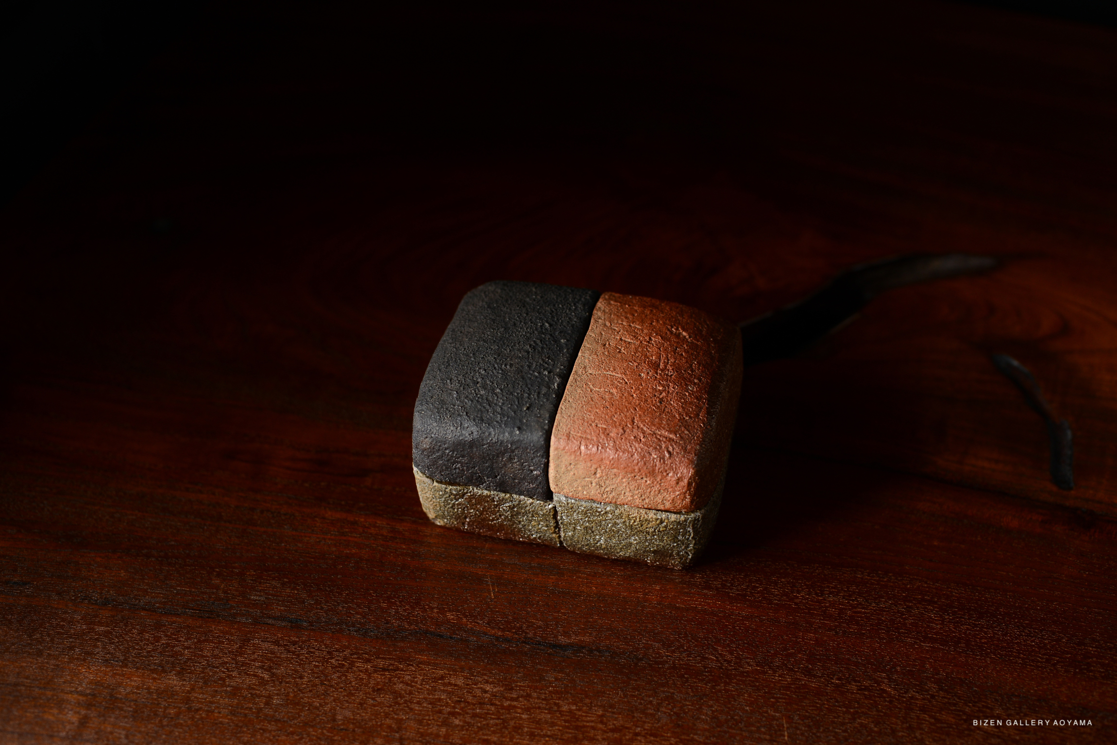 A piece of pottery featuring contrasting colors of dark gray and terracotta, resting on a wooden surface.