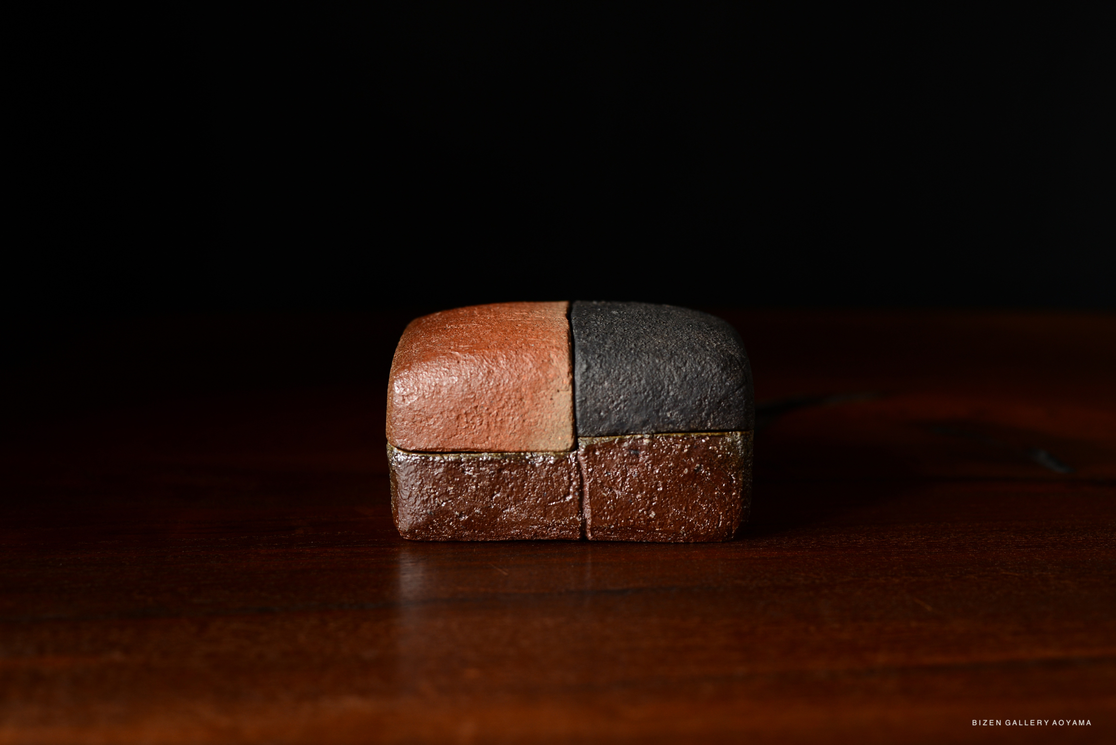 A close-up of a decorative, rectangular ceramic piece with contrasting colors, set against a dark background.