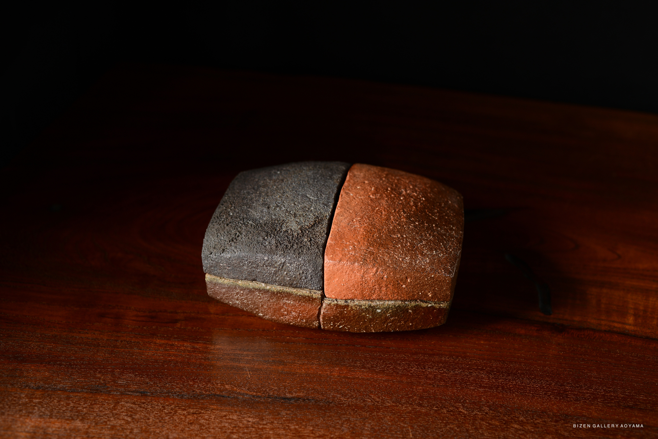 A wooden box with a unique design, featuring a split color of dark and light tones, placed on a polished wooden surface.