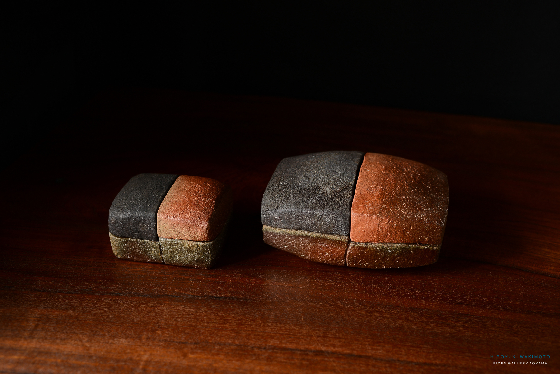 Two uniquely shaped ceramic pieces with a rustic finish on a wooden surface, one larger and one smaller.