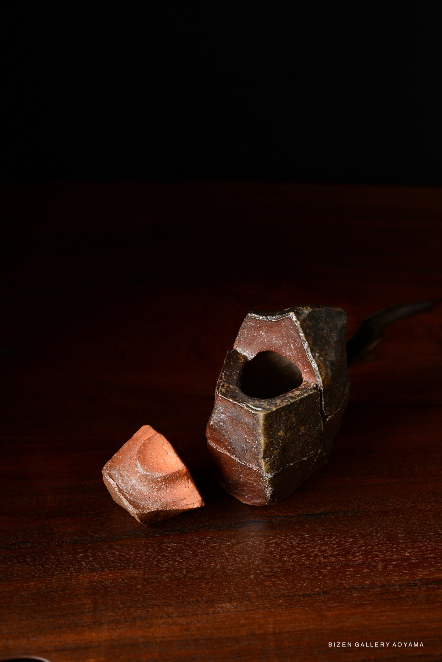 A close-up image of two pieces of ceramic art displayed on a wooden surface, one piece is intact while the other is a broken shard.