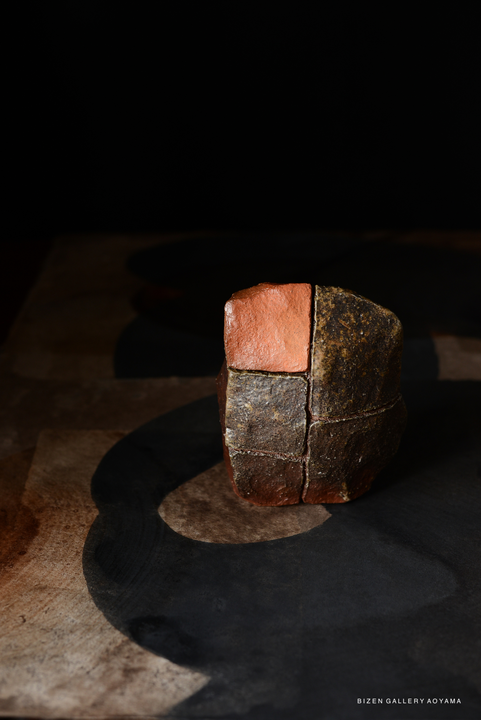 A handcrafted stone sculpture with contrasting textures and colors, placed on a dark, artistic background.