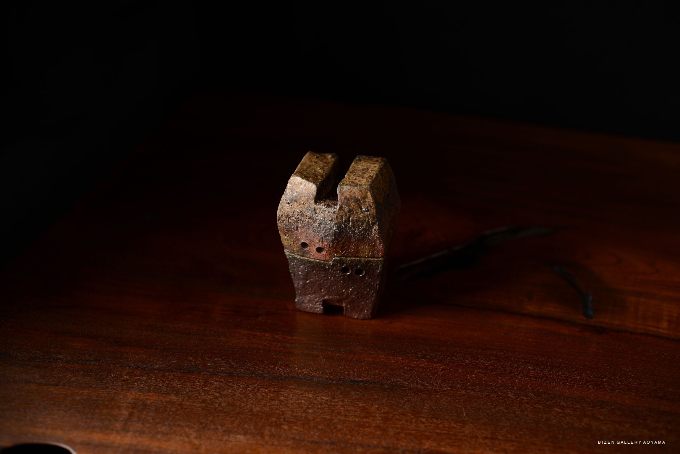 A rustic ceramic object, possibly a traditional tool or decorative piece, displayed on a wooden surface against a dark background.