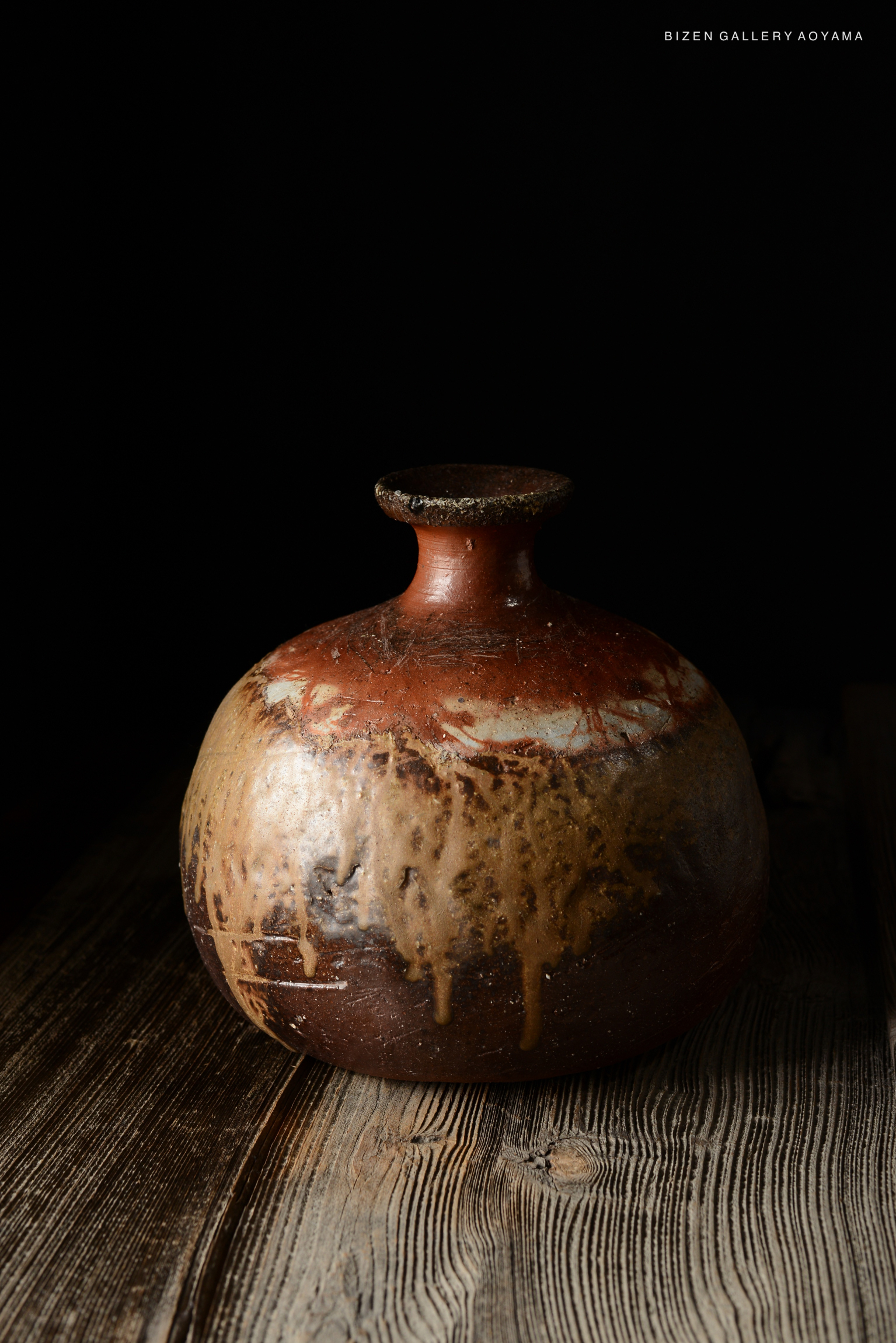 A traditional Bizen pottery tokkuri with a round body and narrow neck, showcasing earthy tones and a textured surface, set against a dark background.