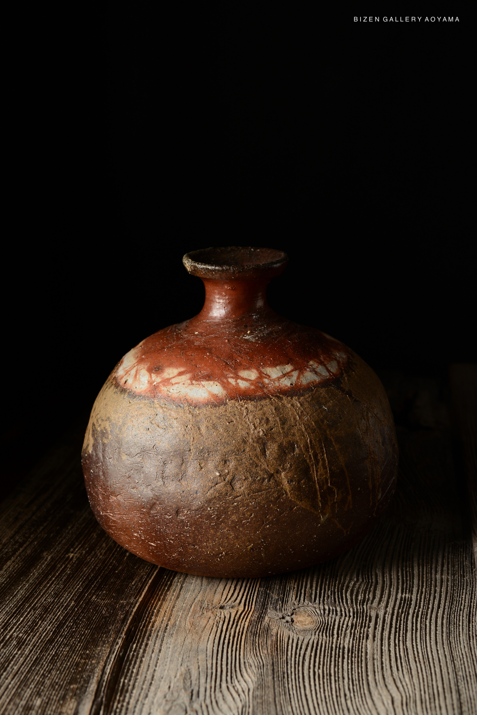 A traditional Bizen pottery Tokkuri with a rounded body and a narrow neck, showcasing earthy tones and a textured surface, set against a dark background.