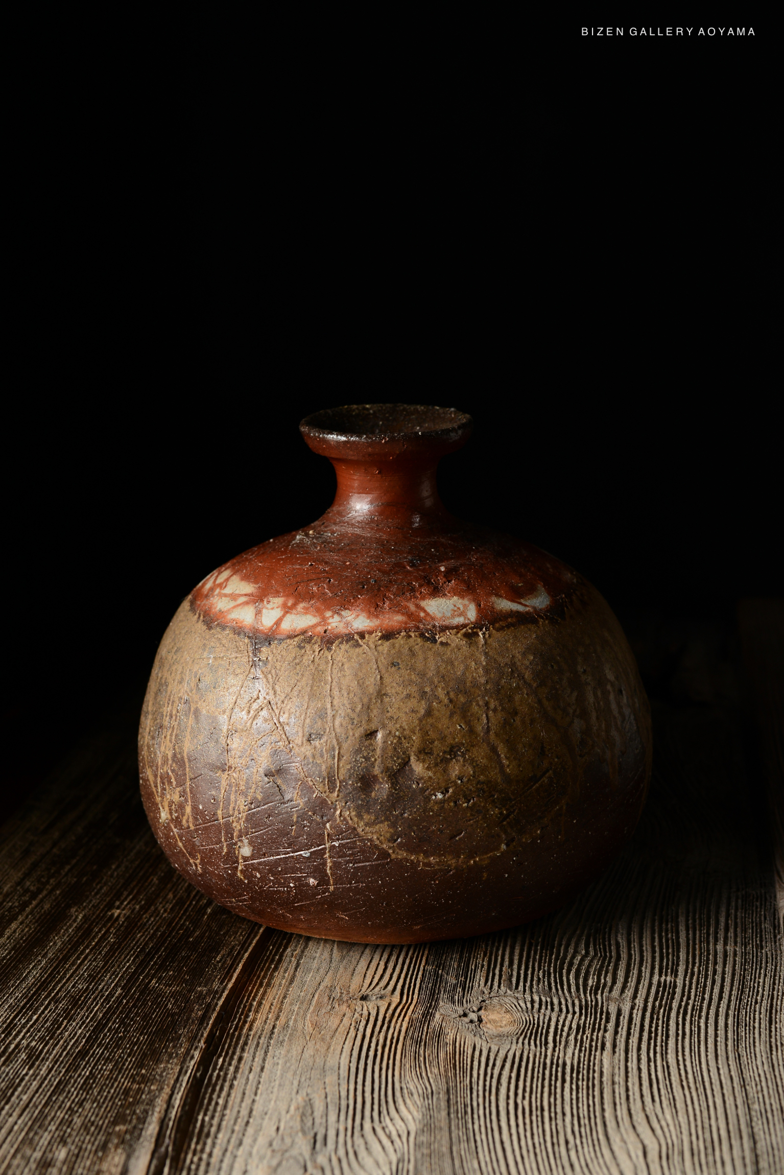 A traditional Bizen pottery tokkuri (sake vessel) featuring a round body and a narrow neck, showcasing earthy tones and textures with a glossy finish.
