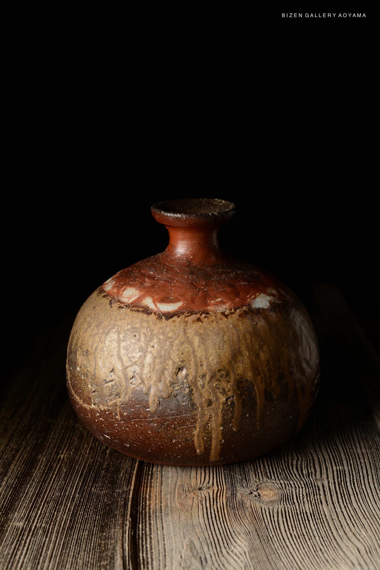A Bizen O Kabura Tokkuri, a traditional Japanese pottery piece, showcased with a rustic, textured surface and a round body, set against a dark background.