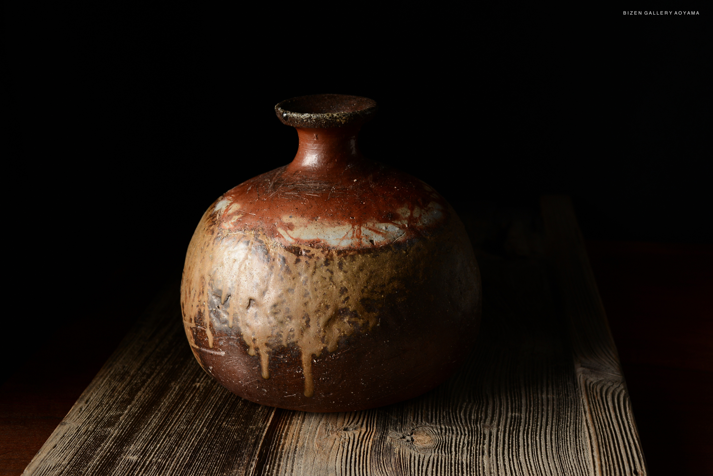 A Bizen O Kabura Tokkuri, a traditional Japanese sake vessel, displaying a rustic brown glaze and unique surface textures, placed on a wooden surface against a dark background.