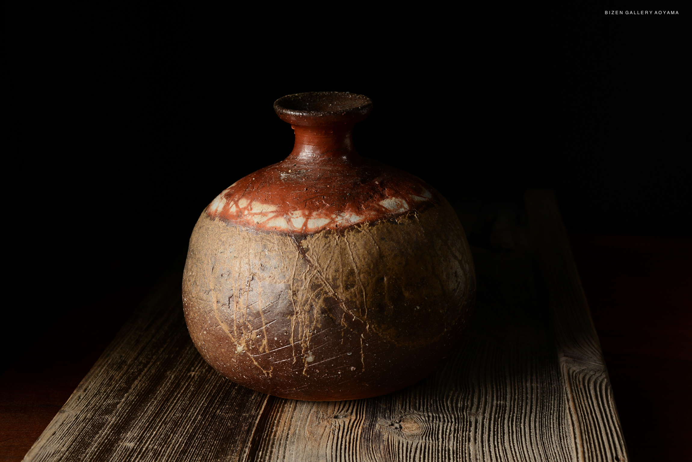 Bizen O Kabura Tokkuri, a traditional Japanese sake vessel, featuring a round body and narrow neck, aged clay with a reddish-brown glaze on a wooden surface.