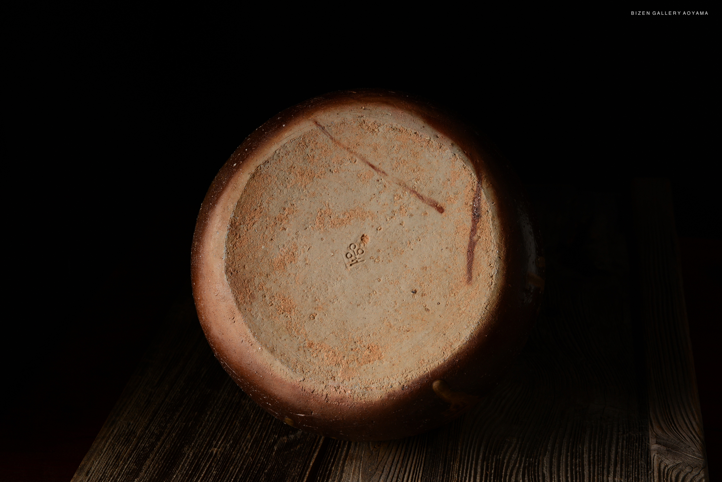 Underside view of a Bizen O Kabura Tokkuri, showcasing its texture and craftsmanship against a dark background.