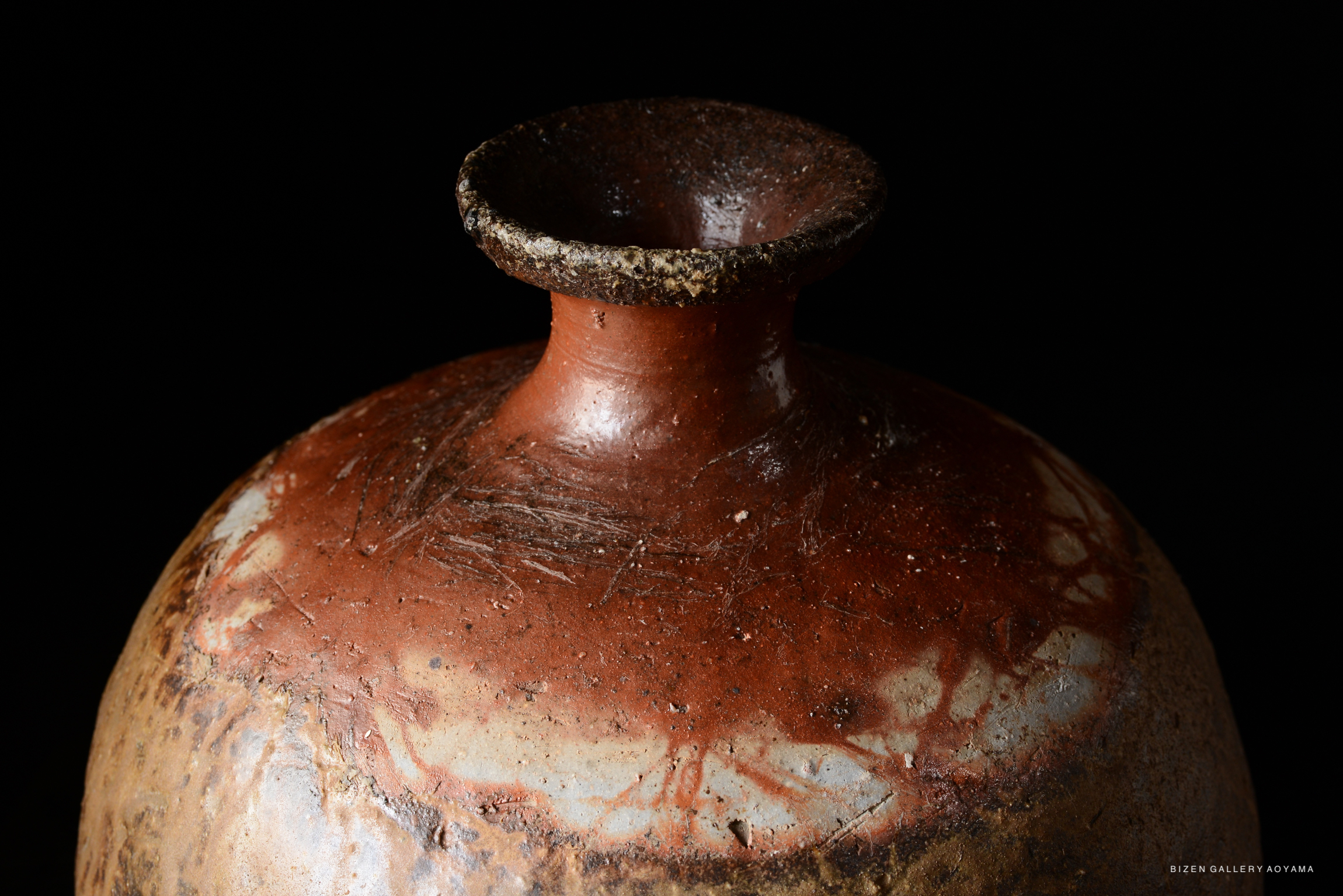 Close-up of a traditional Bizen pottery Tokkuri, featuring a reddish-brown surface with unique textures and a narrow neck.