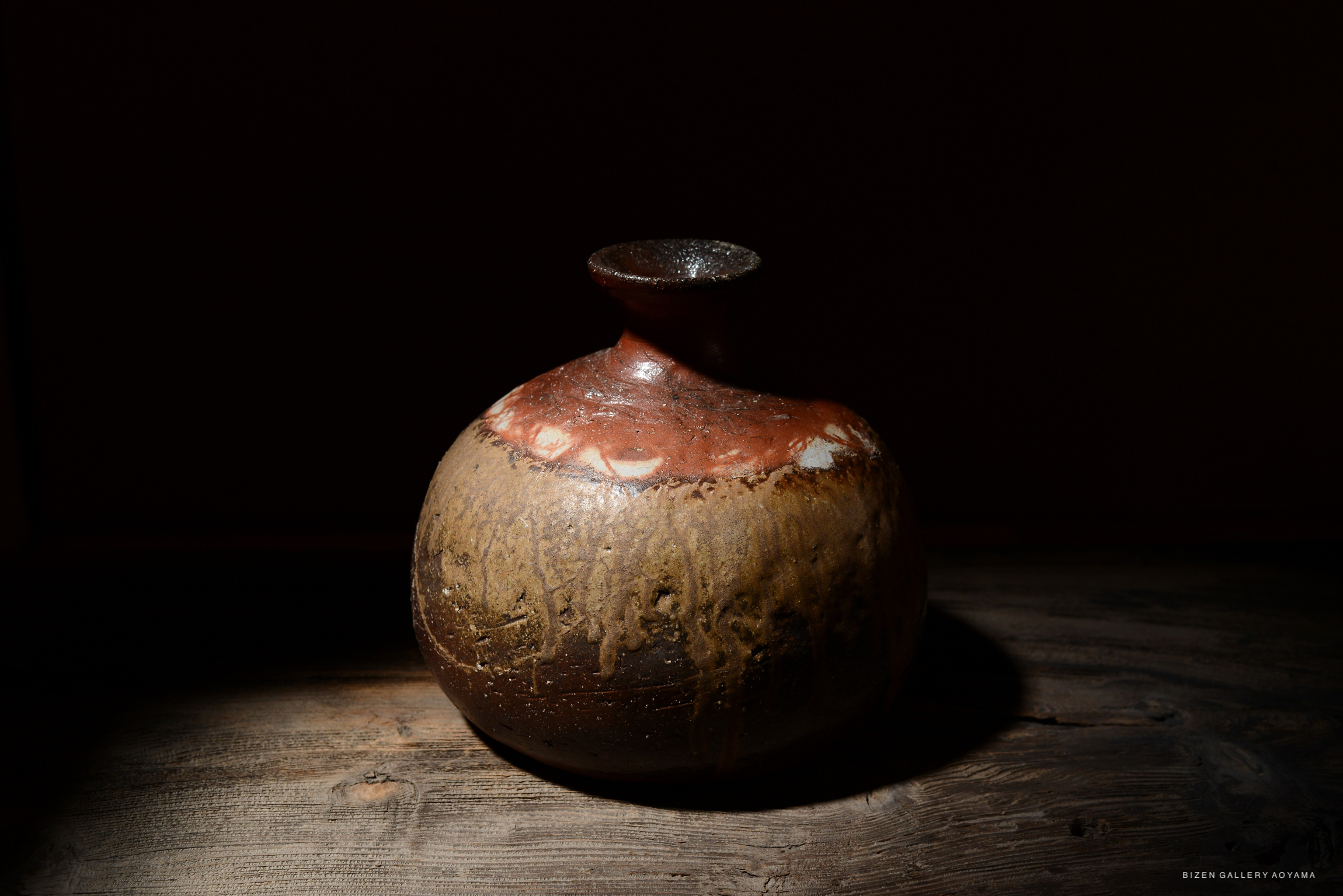 A Bizen O Kabura Tokkuri, traditional Japanese ceramic sake bottle, displayed on a wooden surface with dramatic lighting.