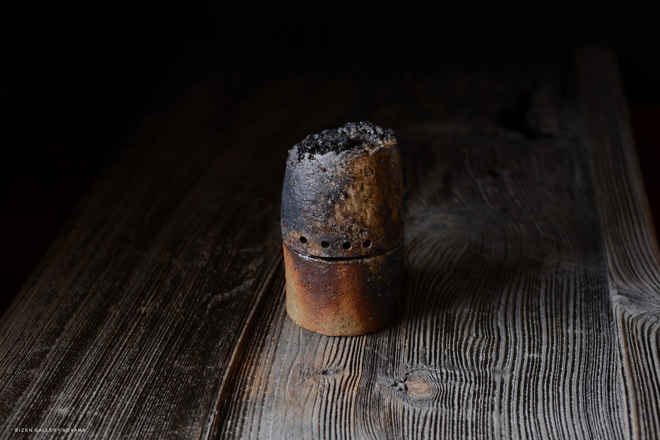 A handcrafted Bizen pottery piece with a textured, burnt surface, displayed on a wooden table.