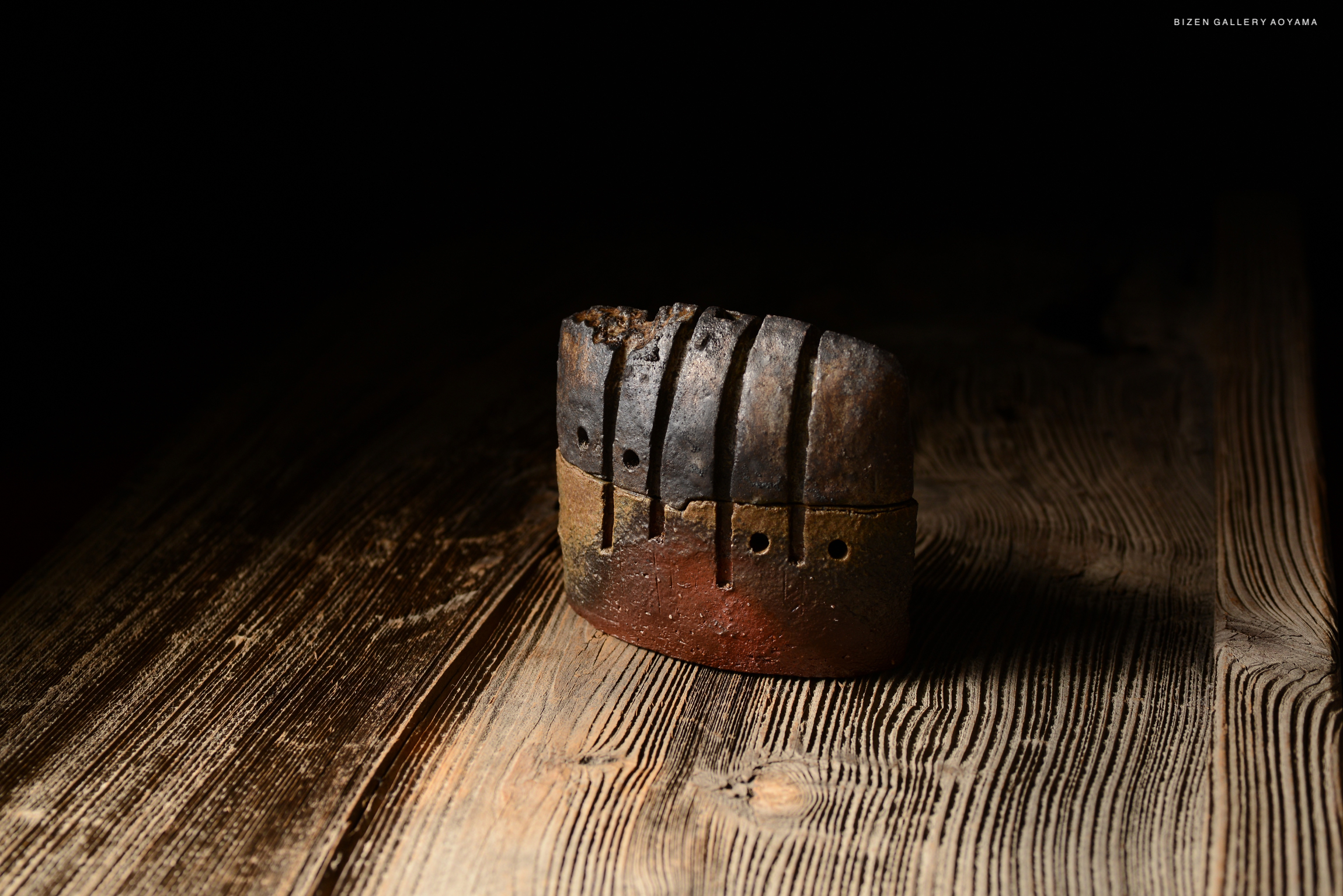 A unique incense burner made from clay, featuring a textured surface with lines and holes, placed on a wooden table.