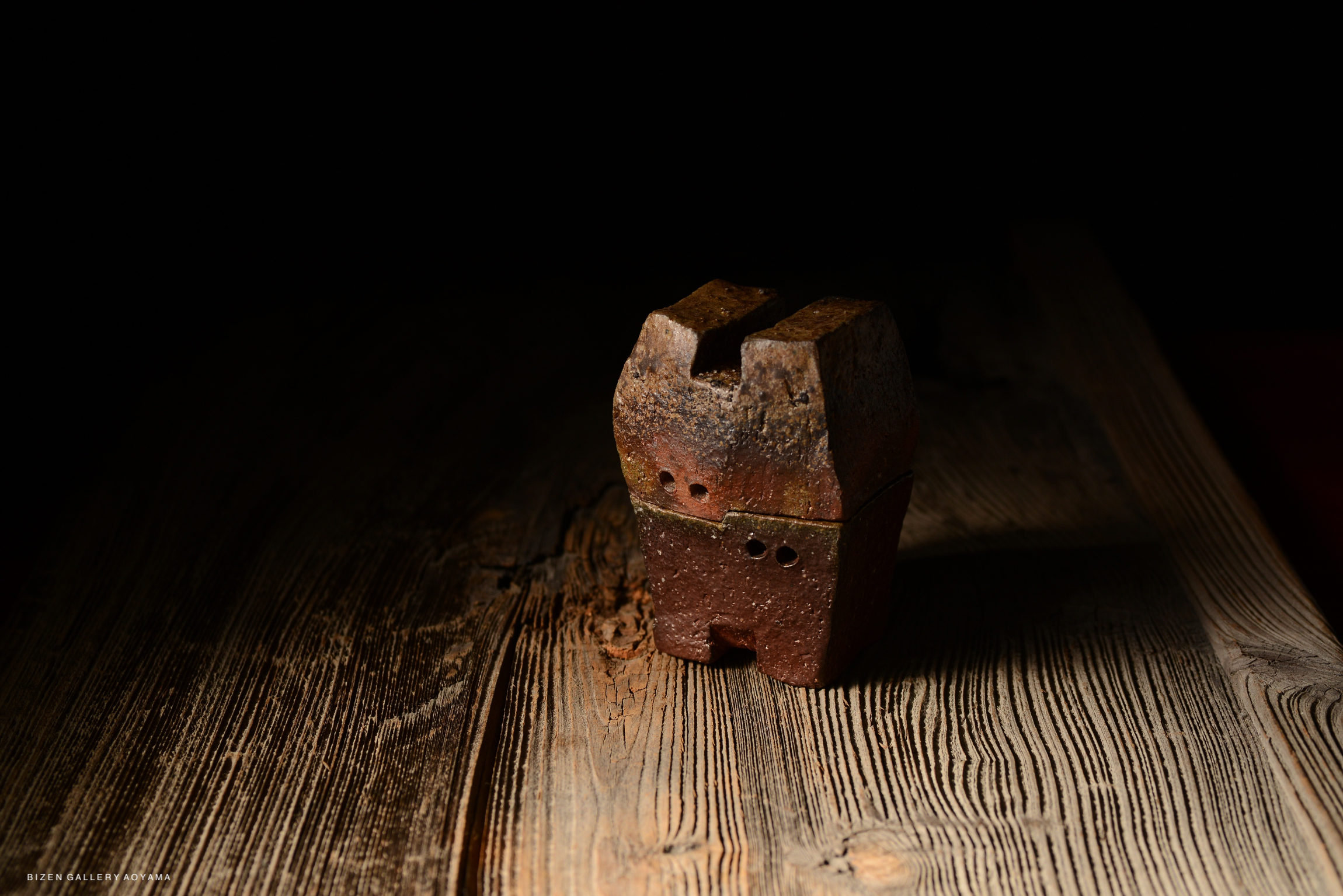 A rustic incense burner with a unique design, placed on a wooden surface, showcasing its texture and color under soft lighting.