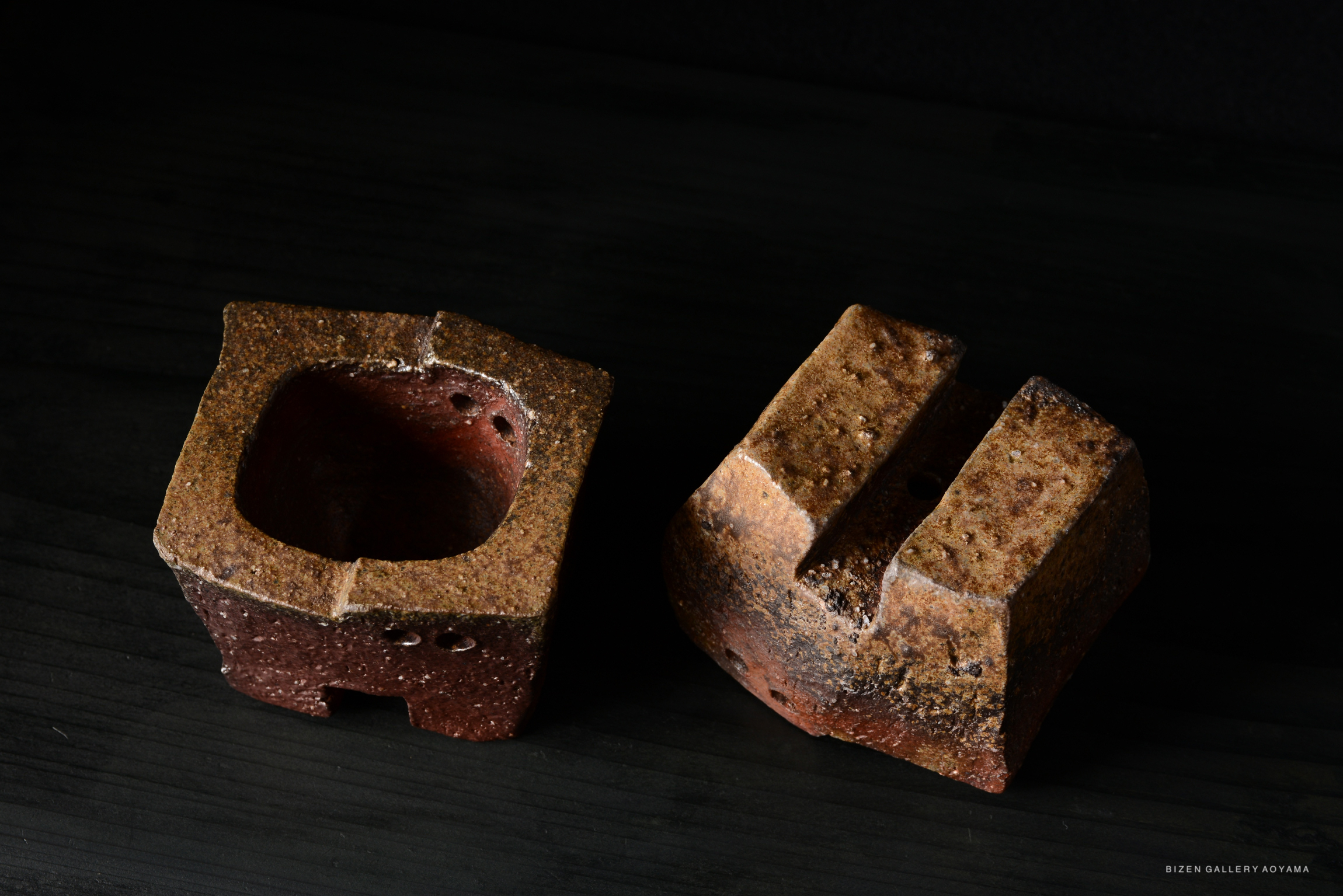 Two unique pieces of Bizen pottery displayed against a dark background, showcasing earthy colors and distinct shapes.