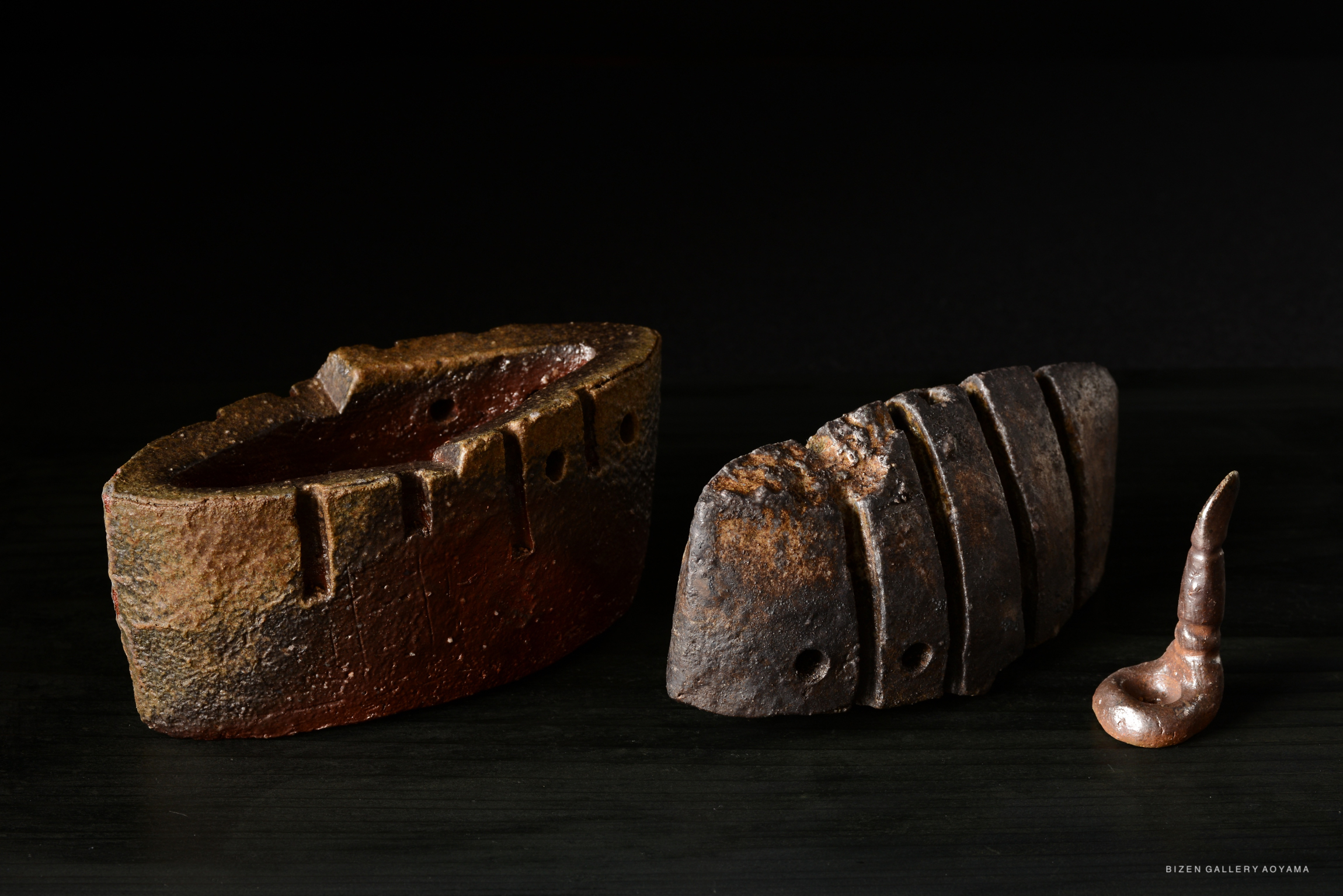 Two ceramic incense burners displayed on a dark surface. The burner on the left has an elongated oval shape with indentations, while the one on the right features a rectangular shape with carved stripes and holes, accompanied by a small decorative piece resembling a curled pipe.