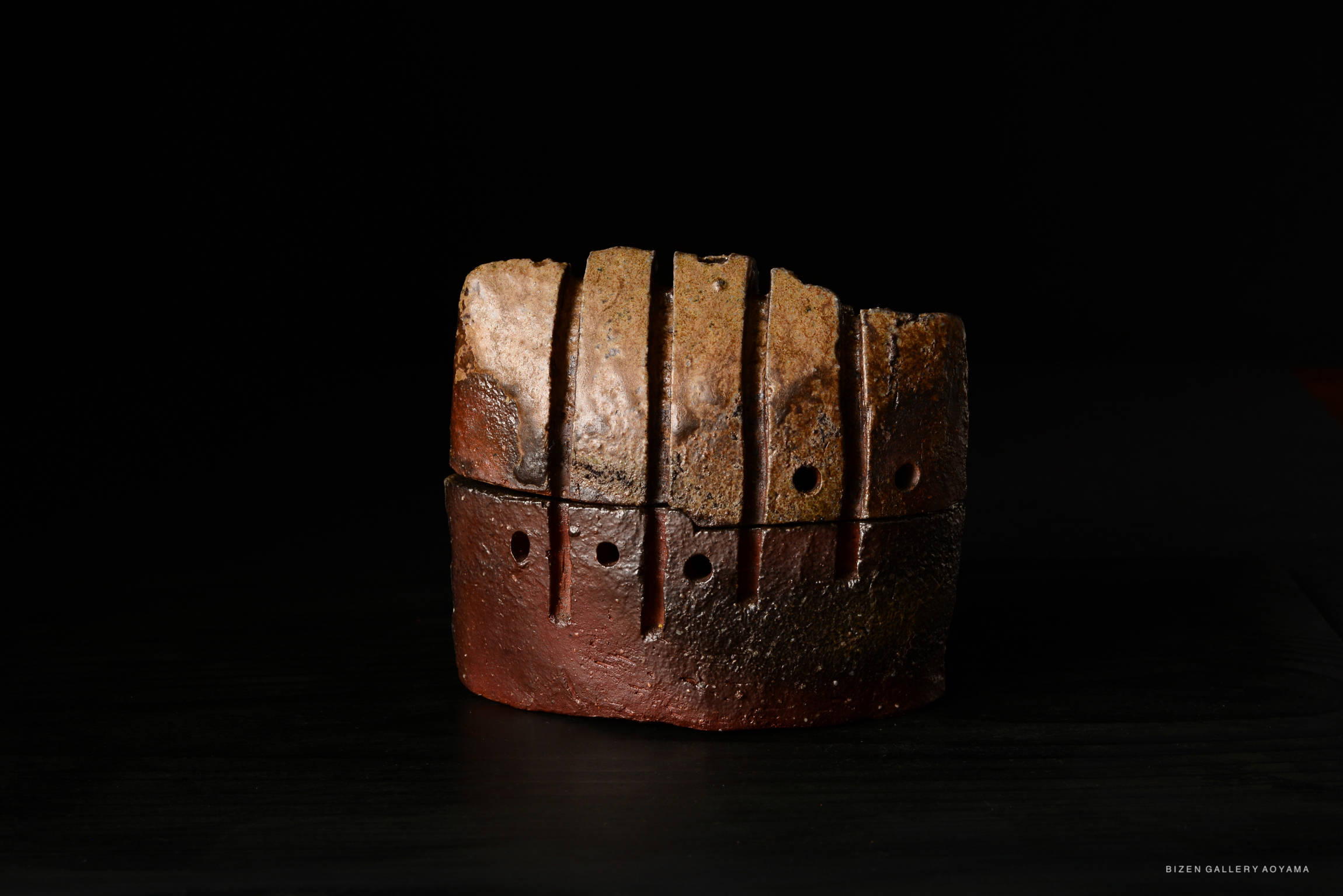 A close-up view of a unique piece of Bizen pottery, showcasing textured surfaces and distinctive irregular shapes, with a dark background.