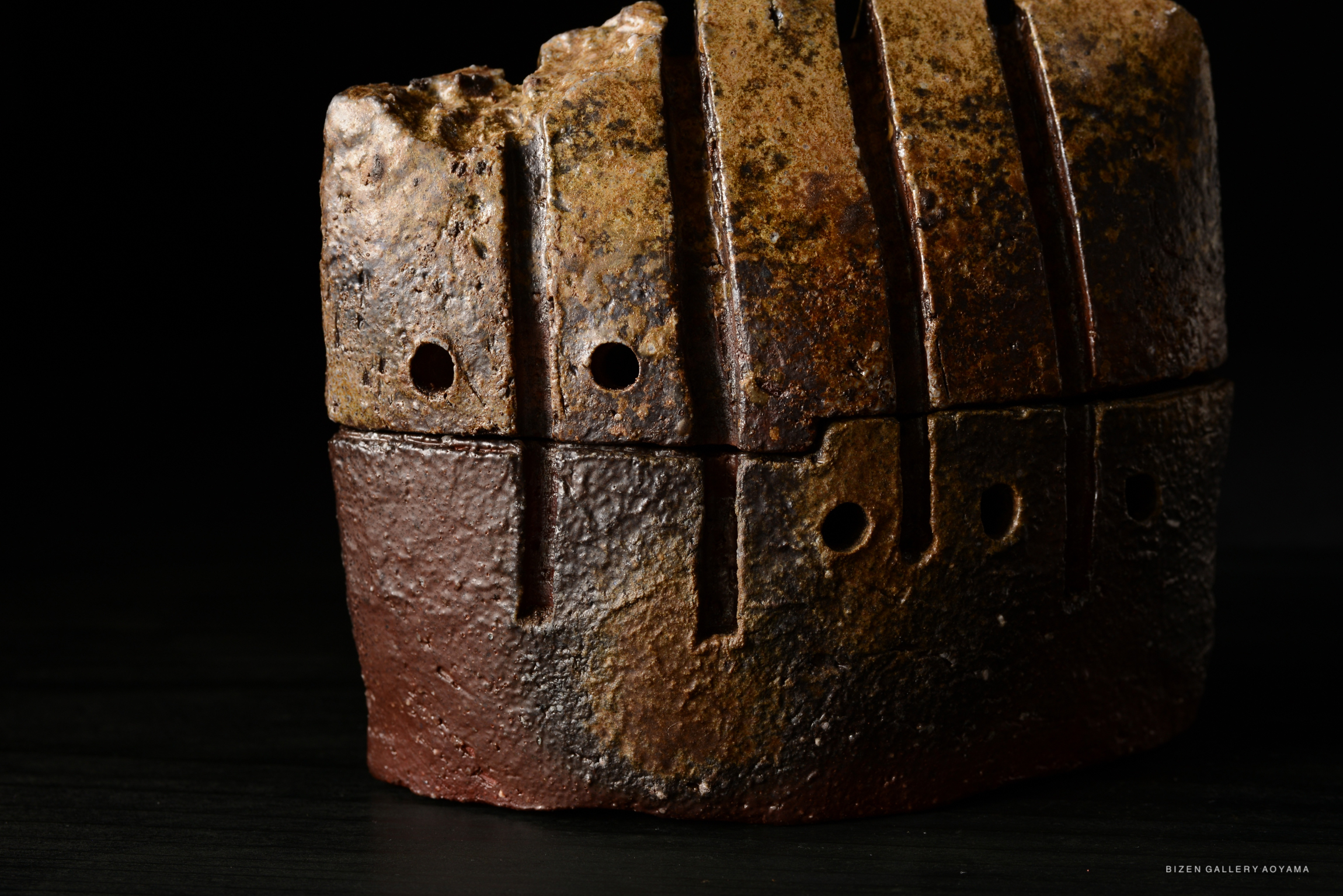 Close-up of a textured pottery piece with a rough surface, featuring dark and earthy tones along with several holes and grooves.