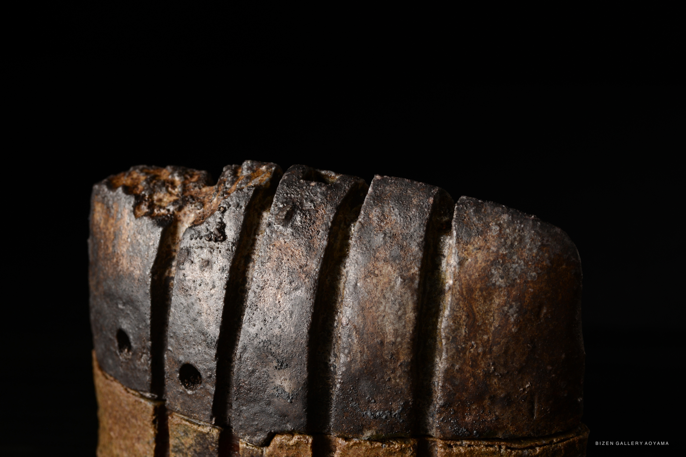 Close-up of an antique incense burner with a textured surface and distinct patterns, set against a black background.