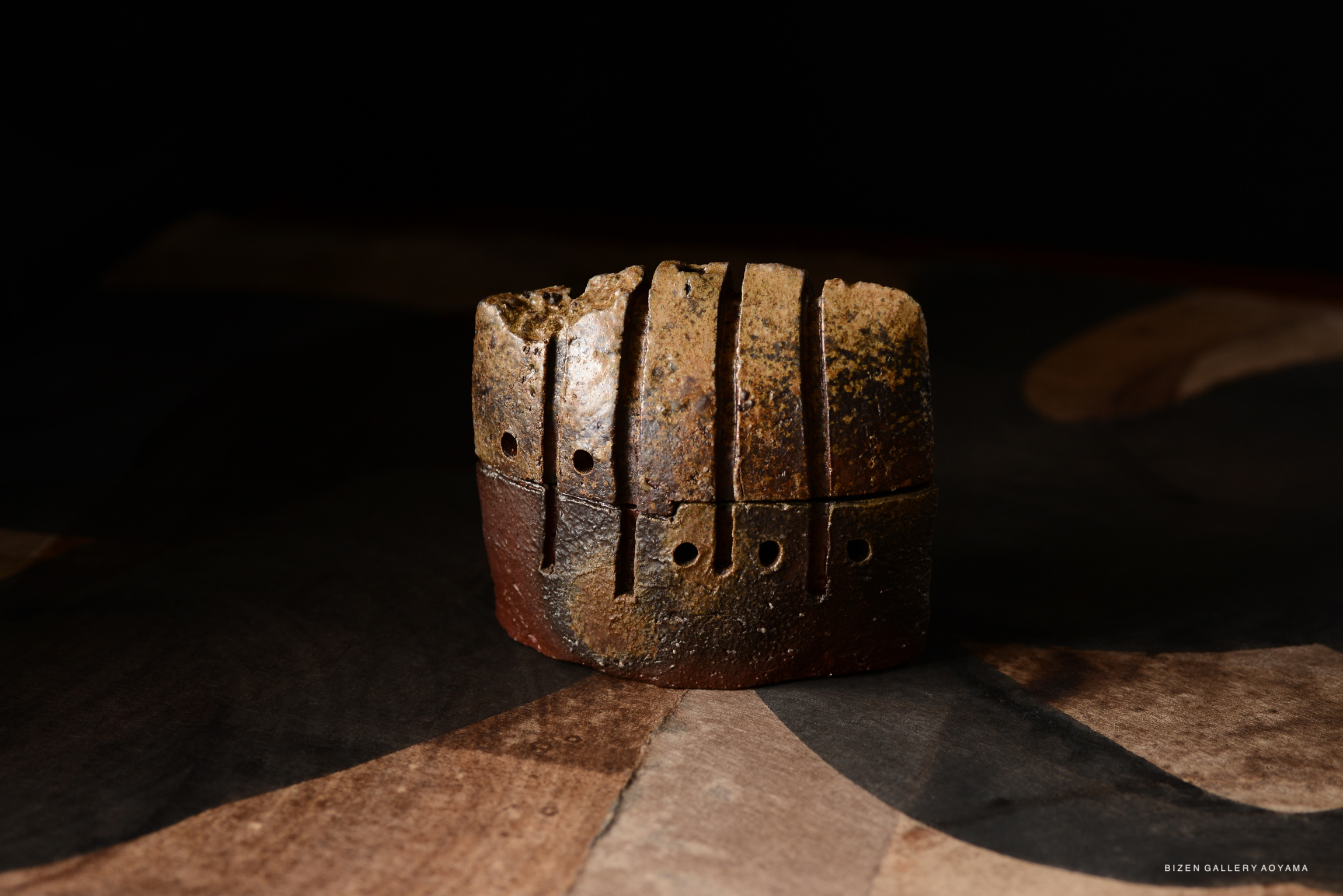 A unique incense burner with textured surfaces and holes, exhibiting earthy tones on a patterned background.