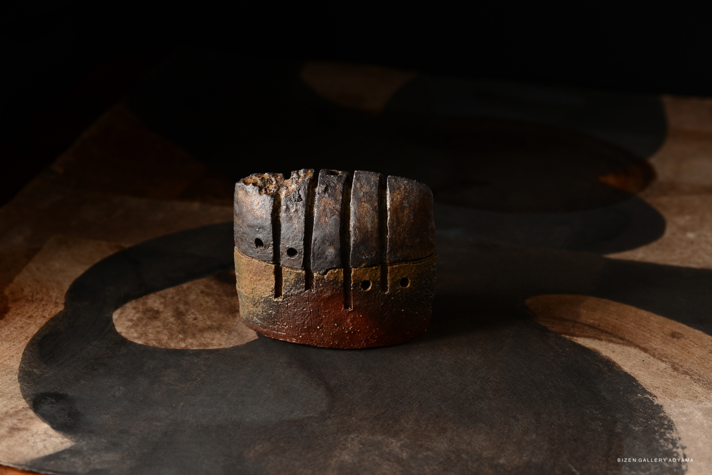 A textured incense burner made from clay, featuring a distinct shape with multiple holes for ventilation, on a dark, abstract background.