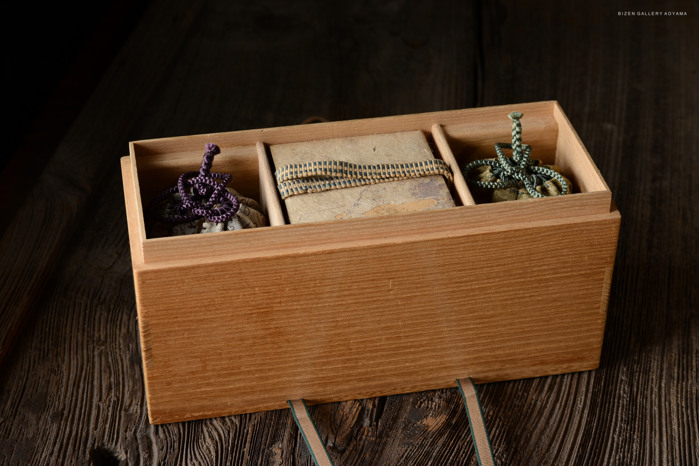 A wooden box containing three compartments, each holding items bound with colorful cords, resting on a wooden surface.