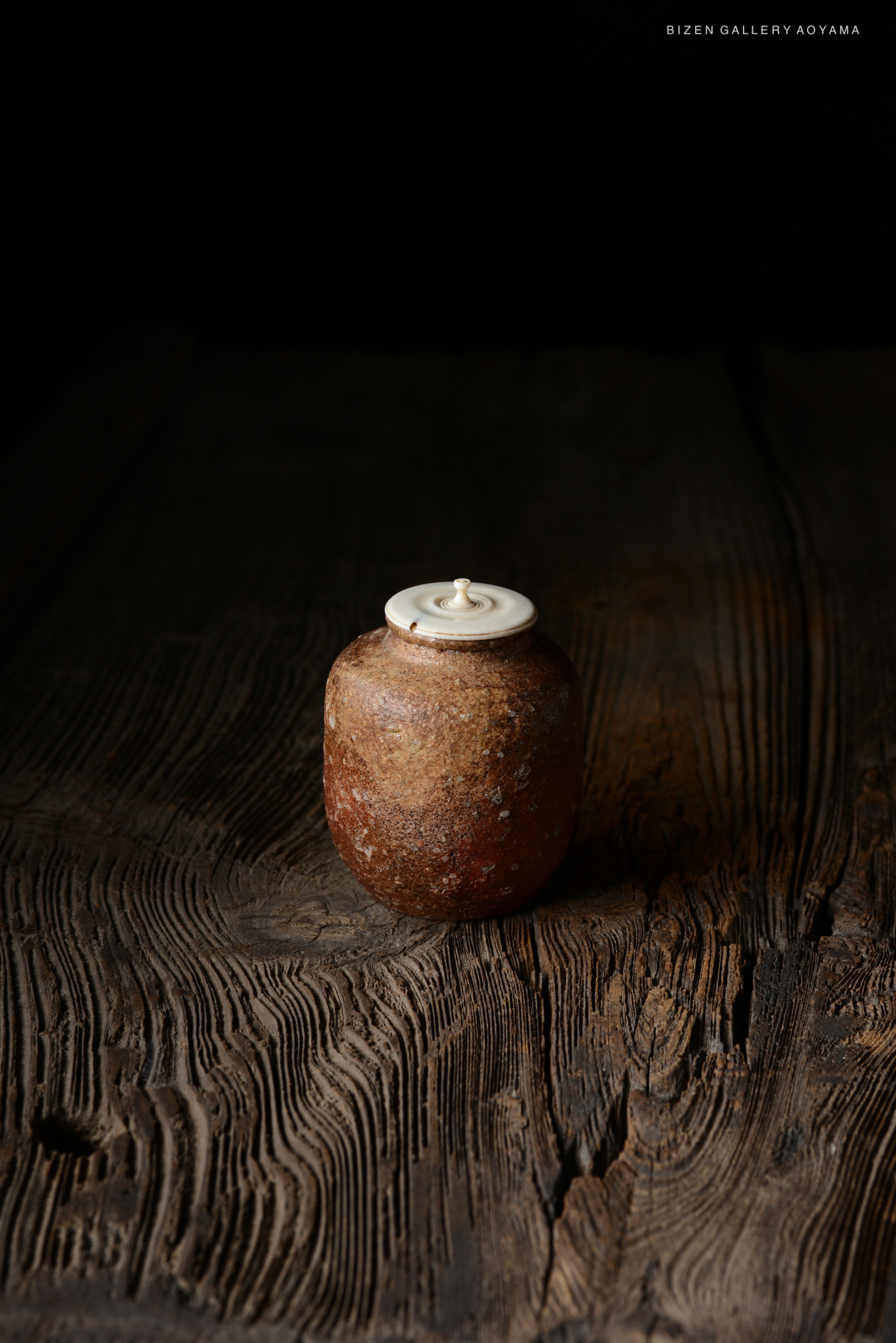 A Shigaraki Chaire with an engraved signature, resembling natural pottery, placed on a textured wooden surface.