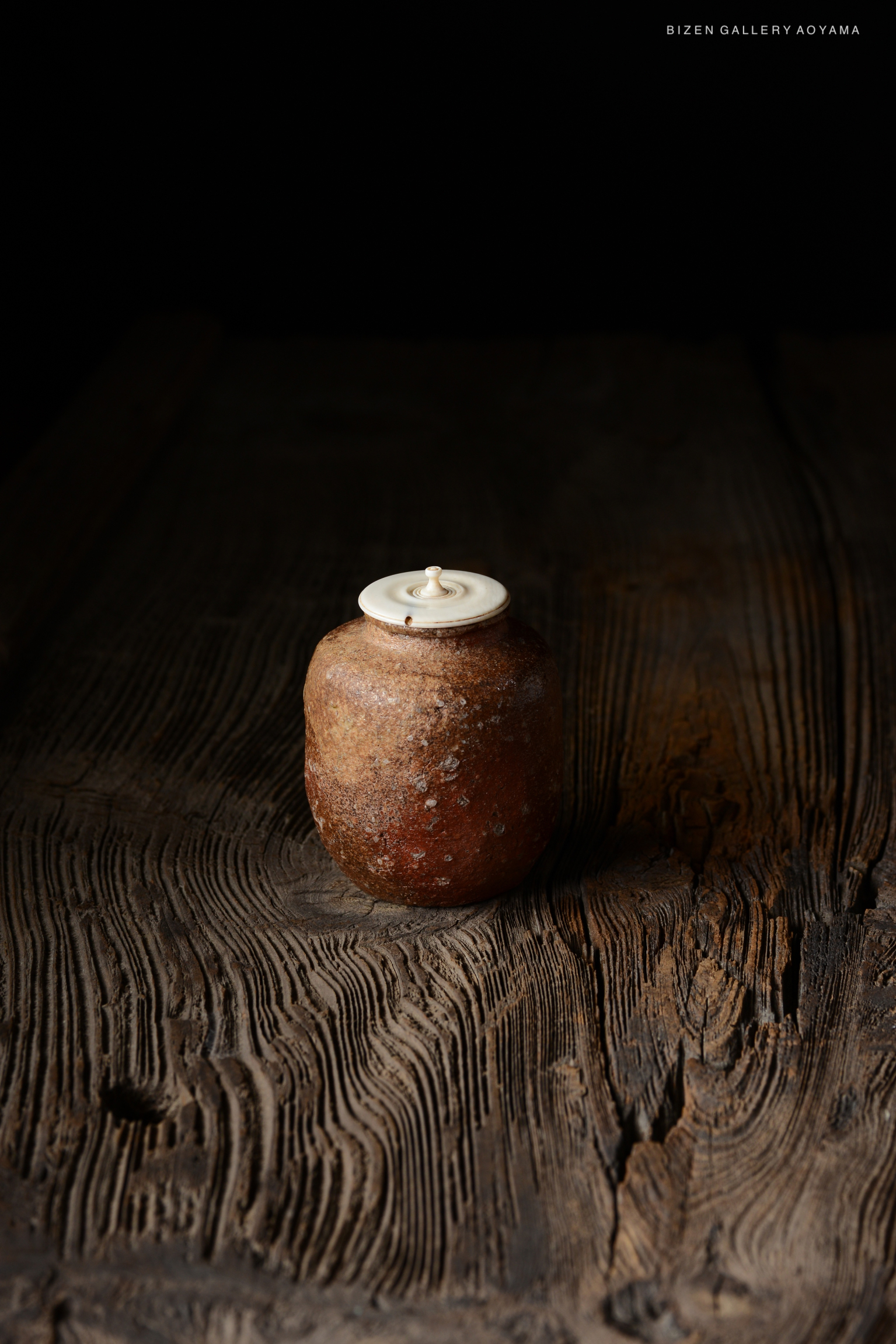 A traditional Japanese tea jar with a round body and a lid, placed on a textured wooden surface.