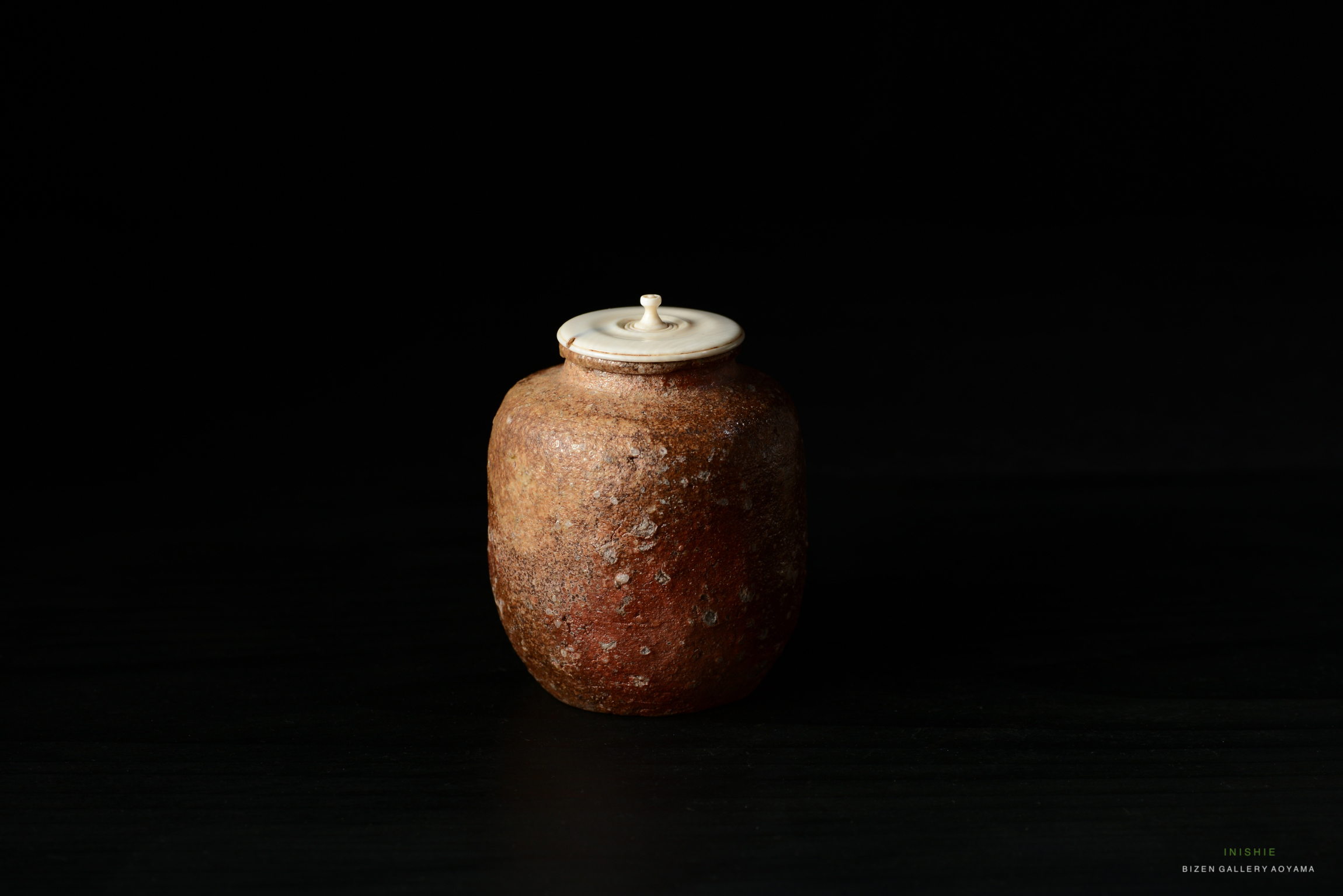 A Shigaraki Chaire adorned with an engraved signature 'Reisetsu', featuring a rounded body with a textured surface, a small lid on top, and set against a black background.