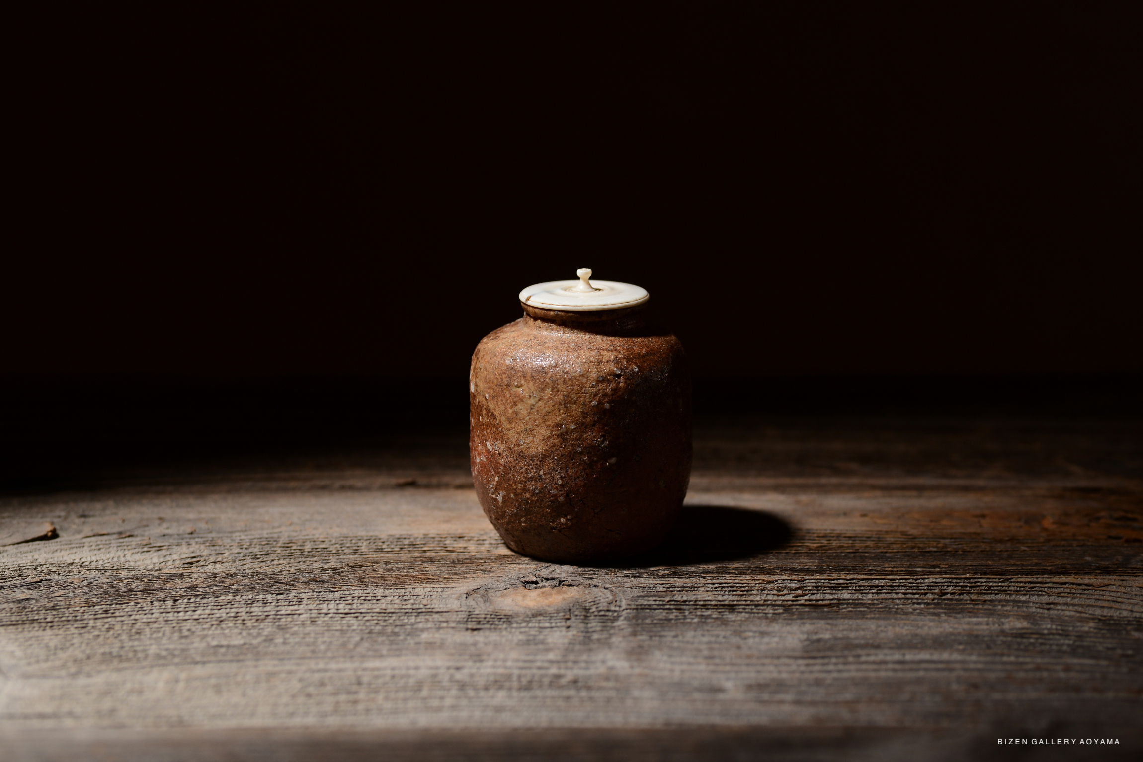 A rustic Shigaraki Chaire tea storage container with an engraved signature and a small lid, set against a dark background on a wooden surface.