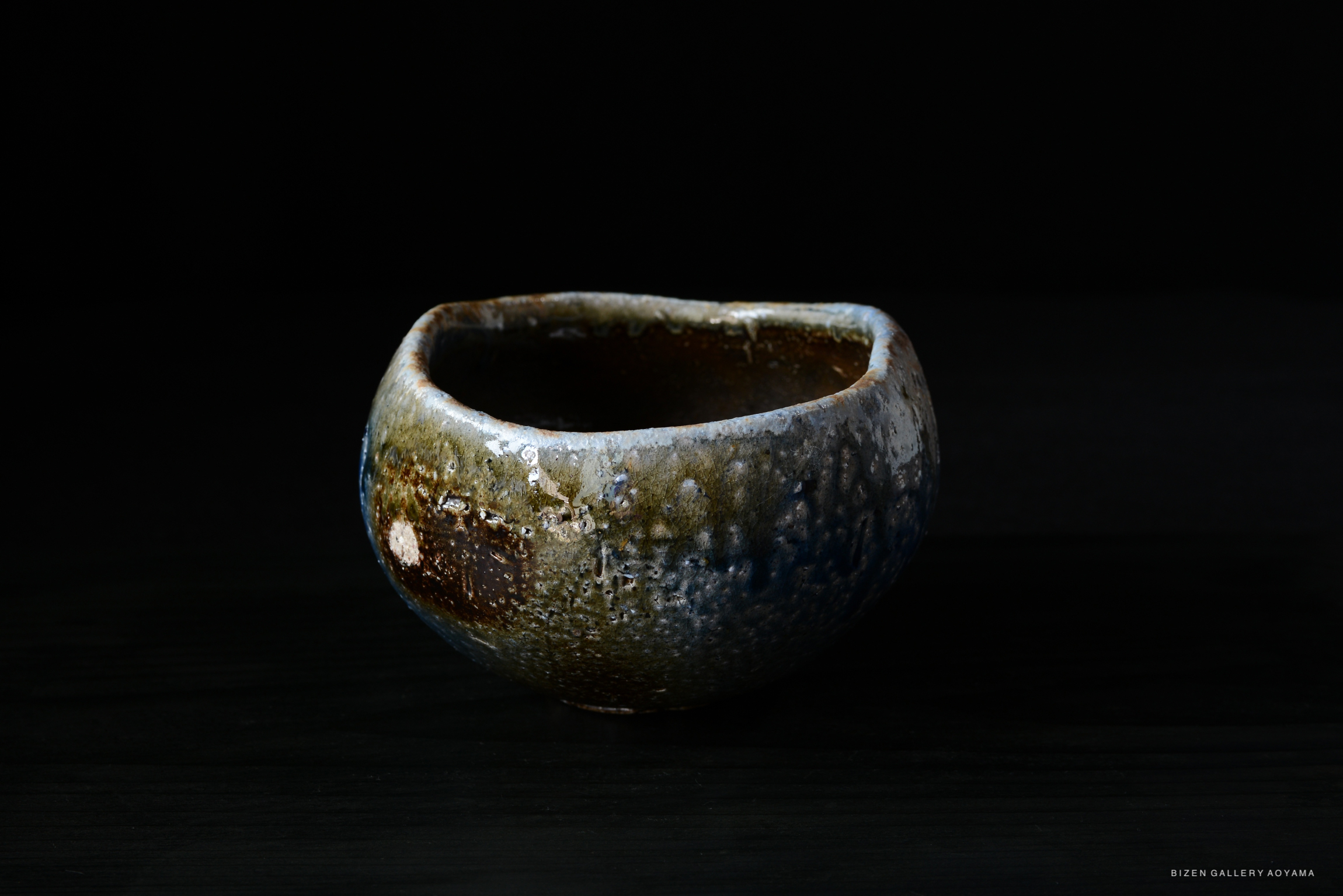A textured ceramic bowl with a glossy surface, featuring shades of blue, brown, and green, placed on a dark background.