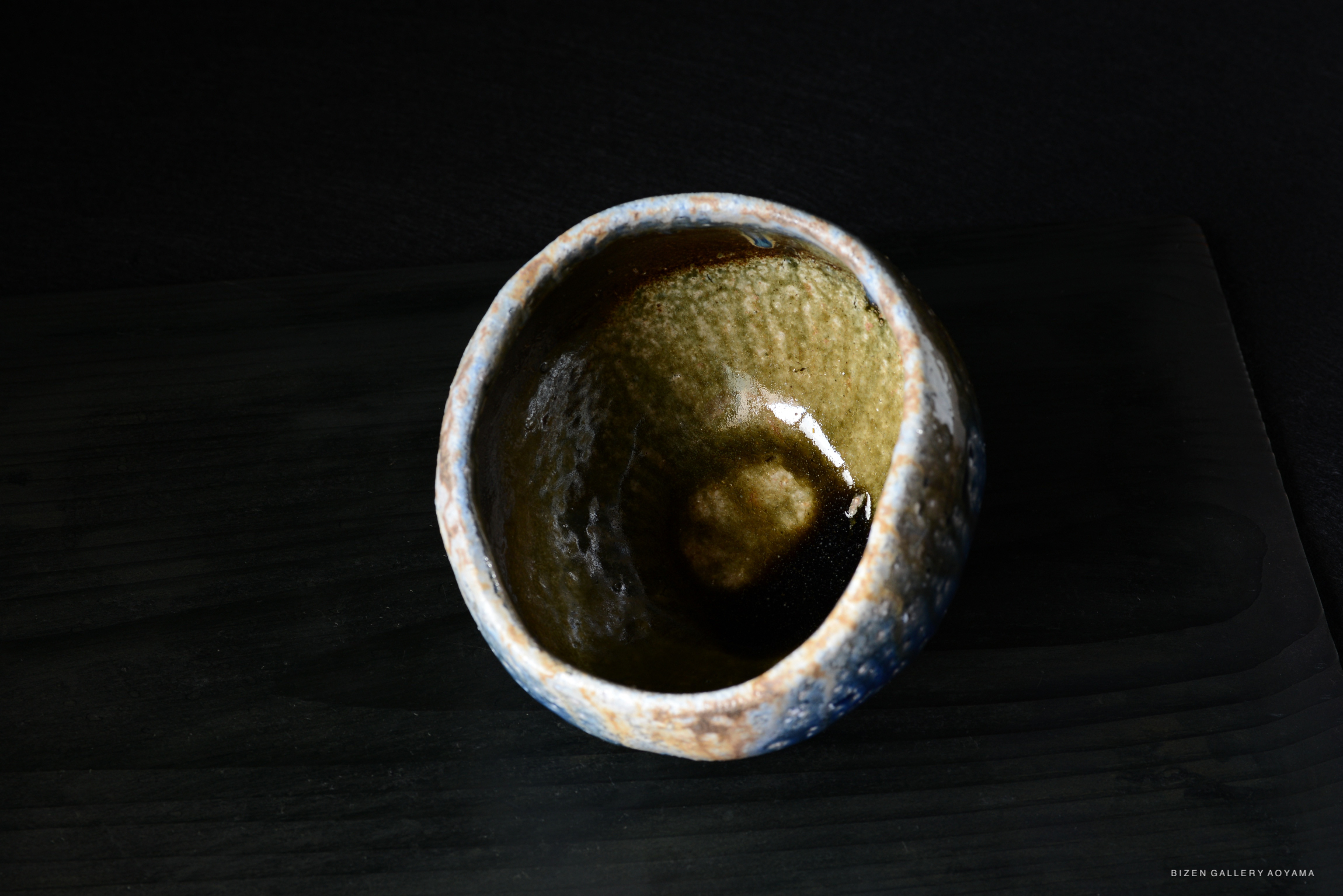 A close-up view of a handmade ceramic bowl with a textured surface and earthy colors, placed on a dark wooden surface.