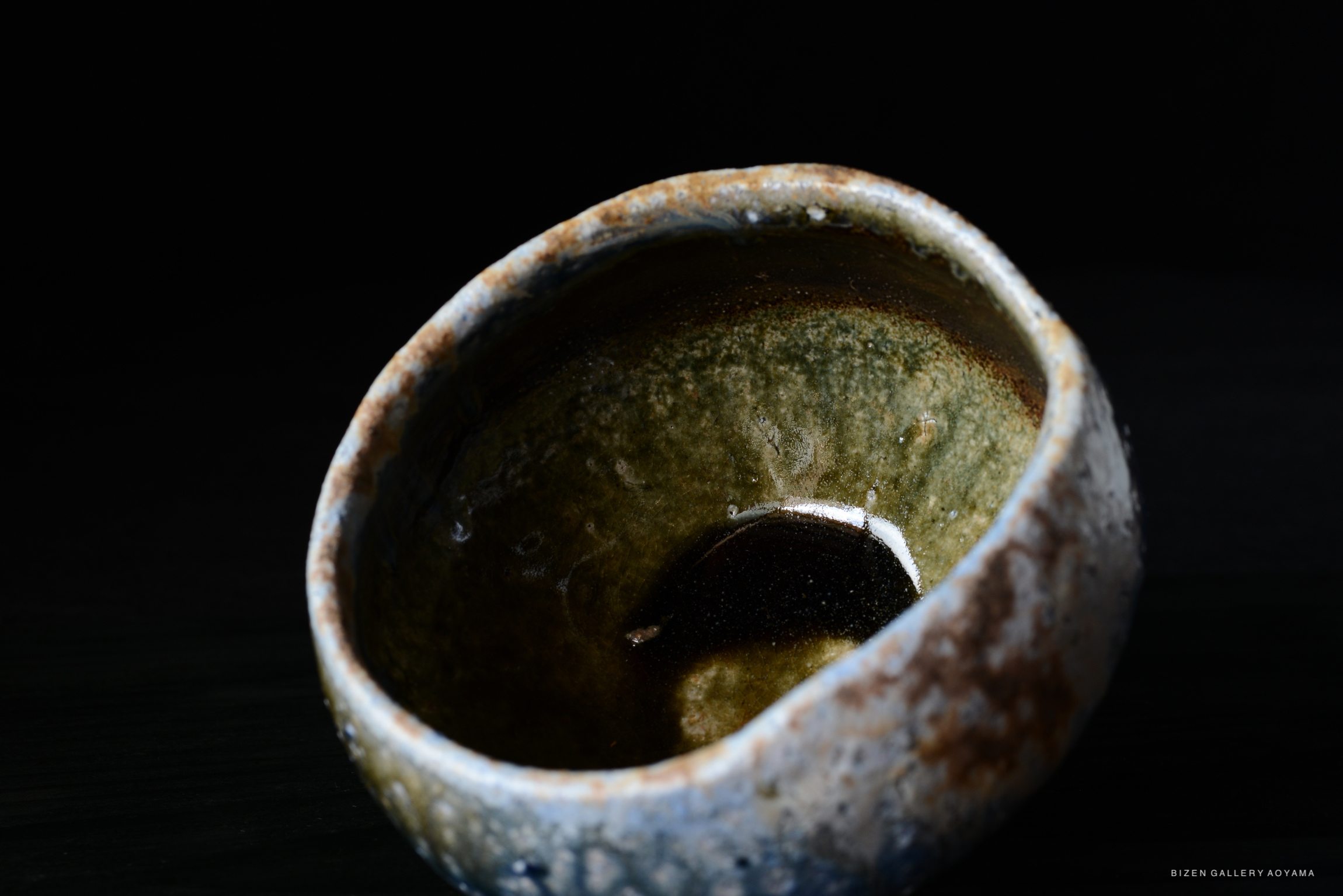A close-up view of a handcrafted ceramic bowl with a textured surface and a mix of earthy colors, placed against a dark background.