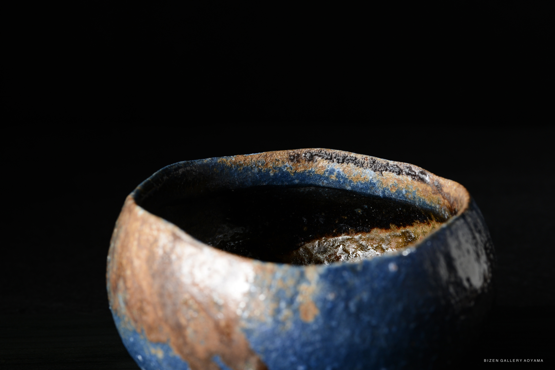 Close-up of a handcrafted pottery bowl with a blue and brown glaze against a dark background.