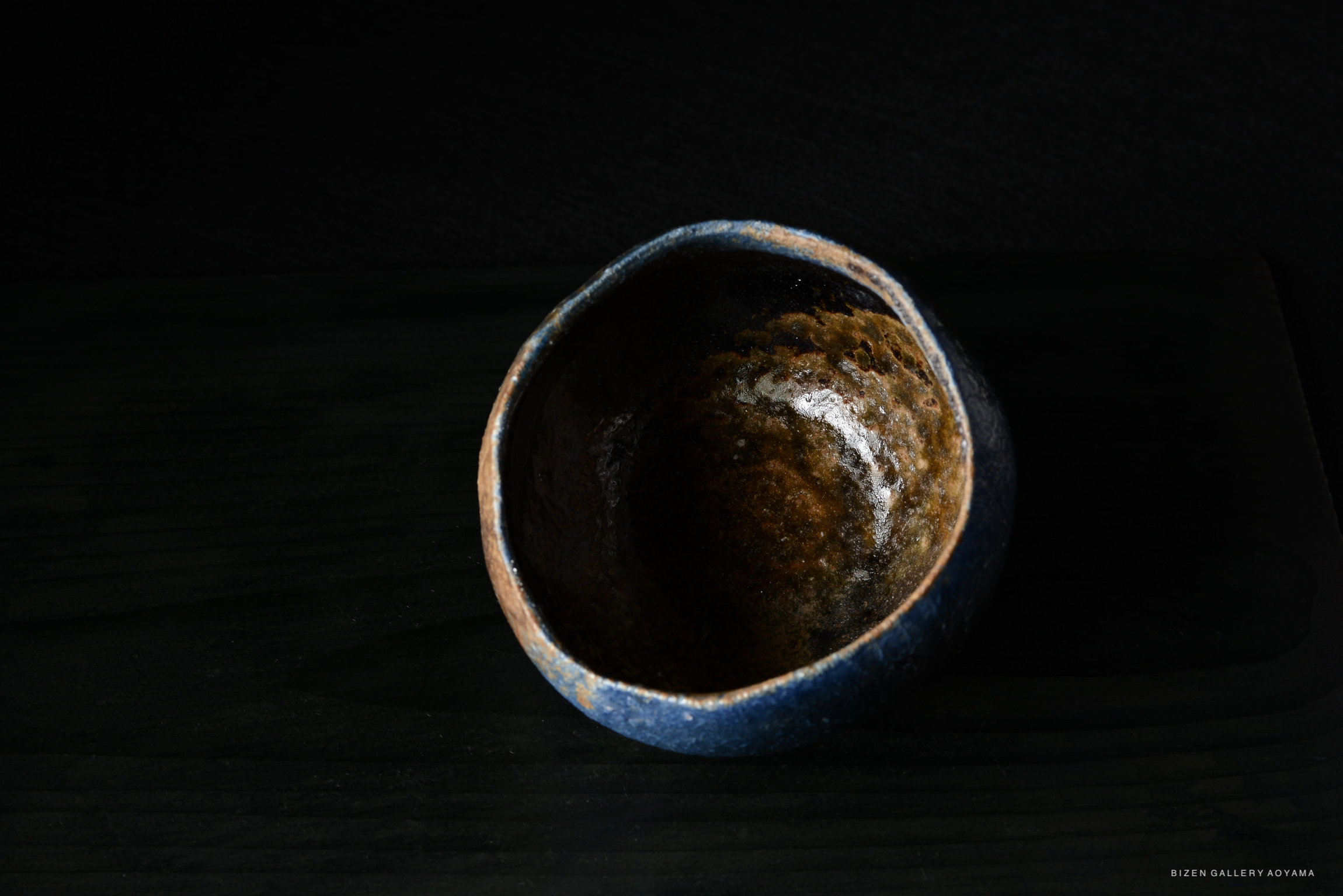 Artistic pottery bowl with a glossy blue exterior and a textured brown interior, set against a dark background.