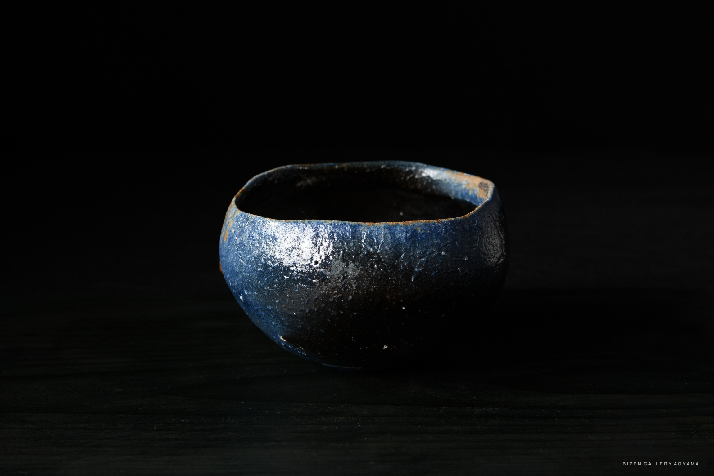 A round ceramic bowl with a textured surface, featuring dark blue and black colors, set against a black background.