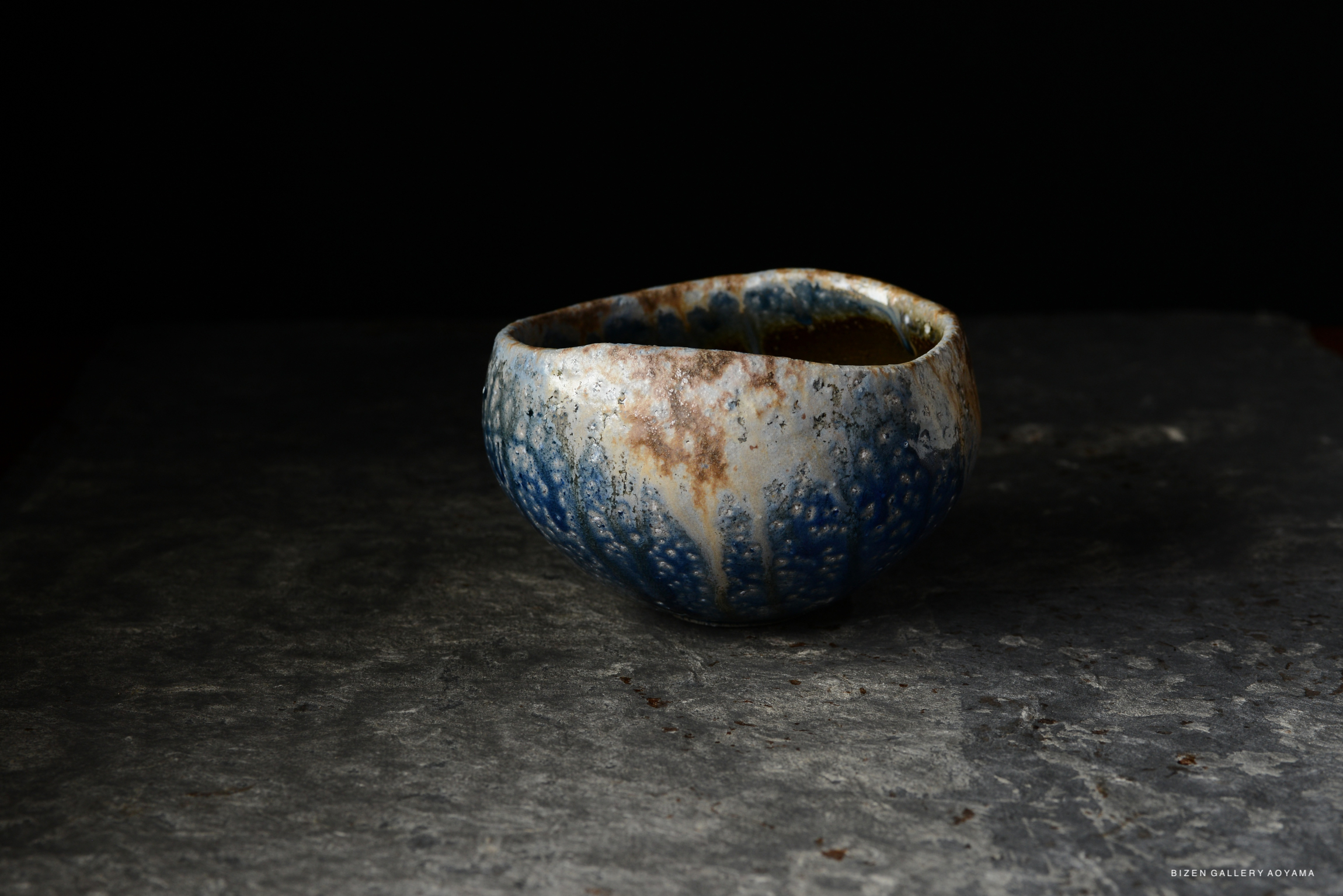 A textured ceramic bowl with blue and earthy tones, positioned on a dark surface against a black background.