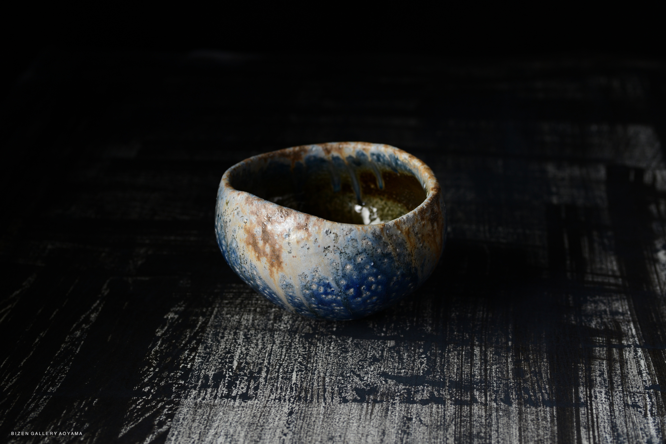 Ceramic bowl with a textured surface and a mix of blue and earthy tones, placed on a dark textured background.