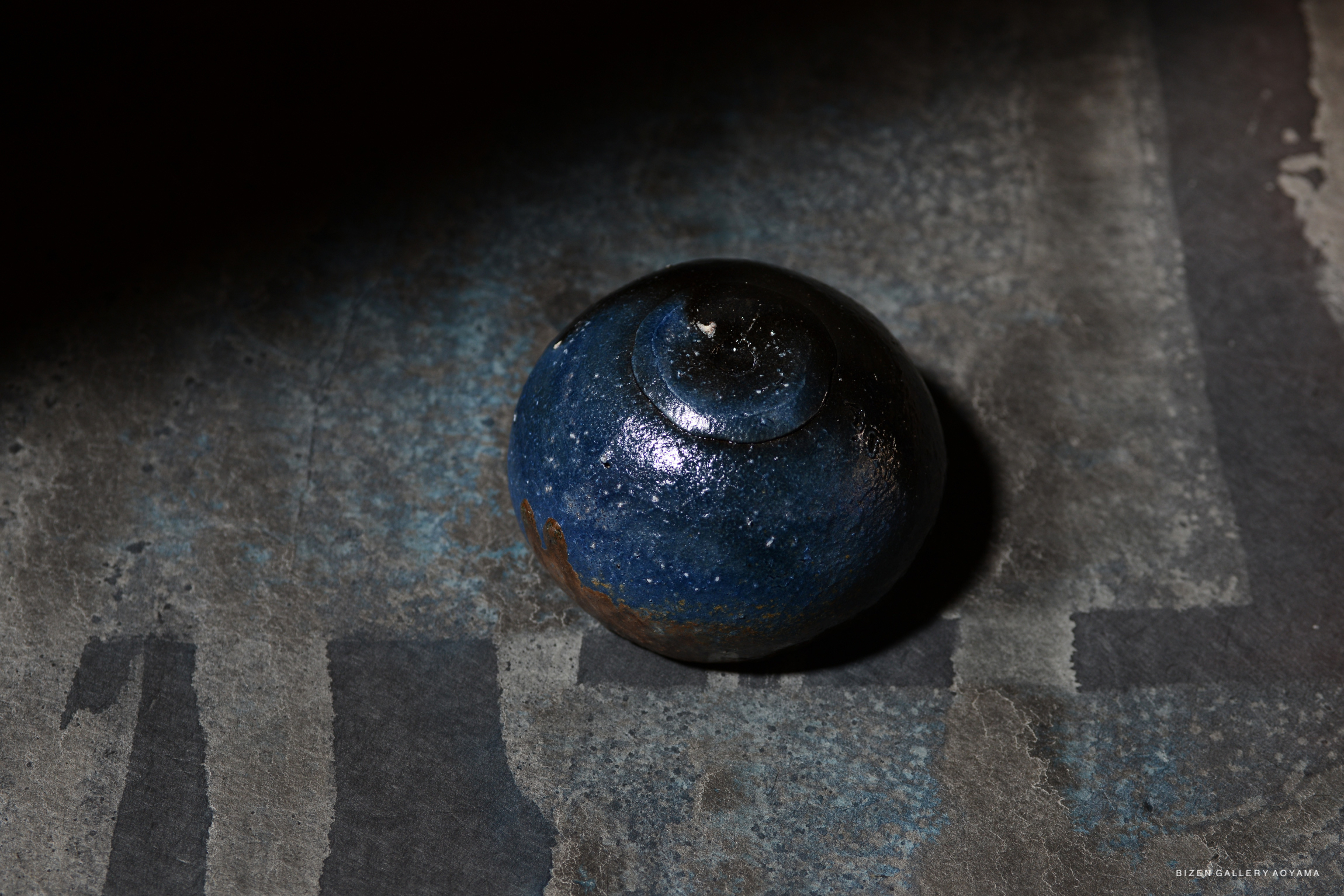 A close-up of a blue ceramic bowl with a glossy finish, placed on a textured surface.