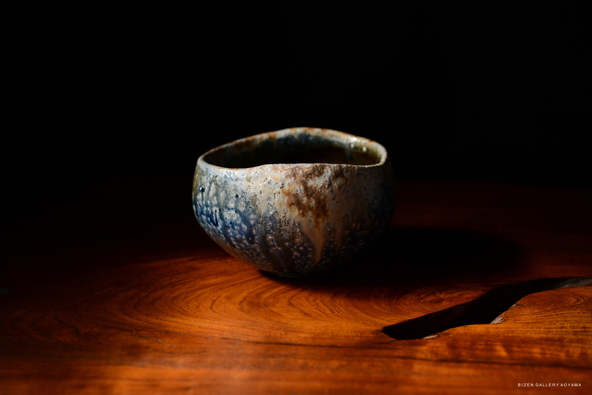 A ceramic bowl with a textured surface and blue glaze, placed on a wooden table under soft lighting.