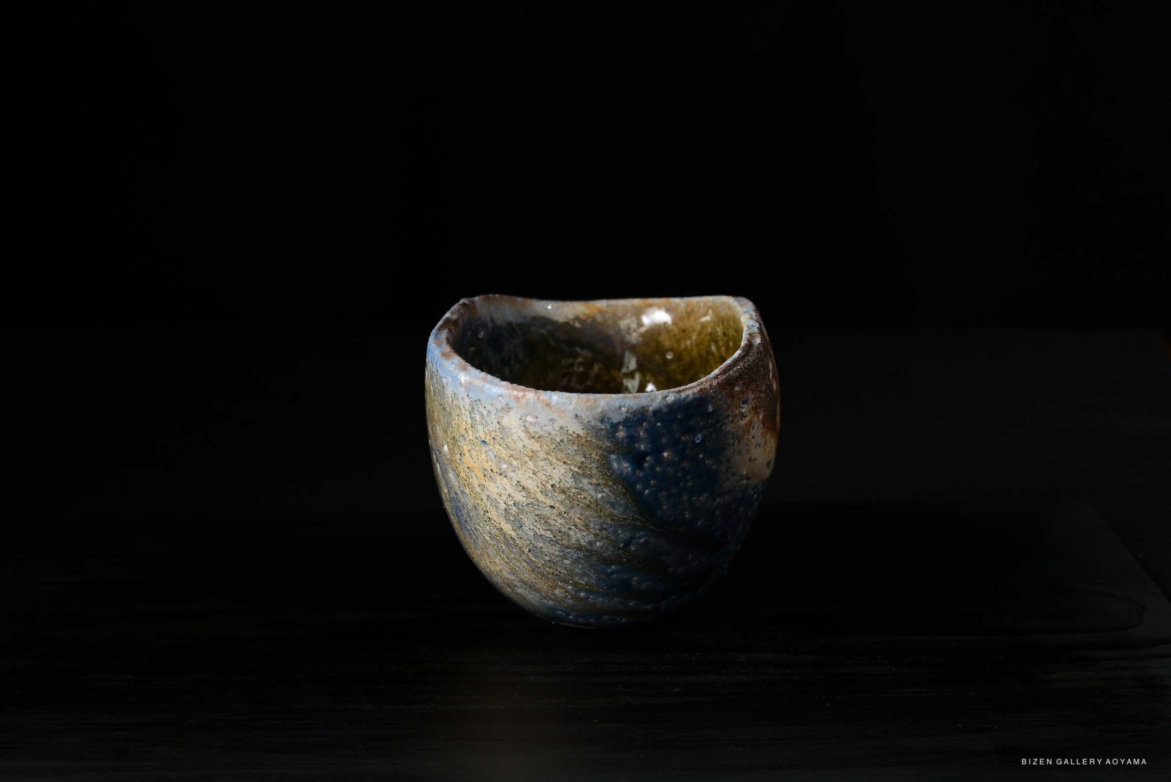 A close-up image of a handcrafted ceramic bowl with an organic shape, showcasing a blend of earthy colors and textures against a dark background.