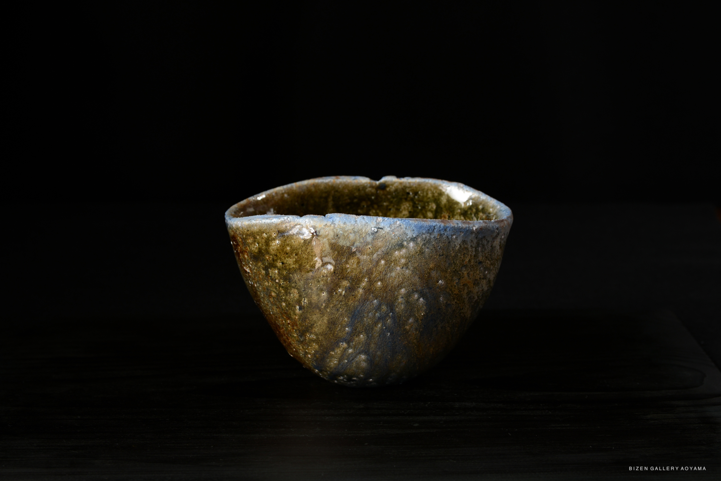 A handcrafted ceramic bowl with a unique textured surface, featuring earthy tones and an irregular shape, set against a dark background.