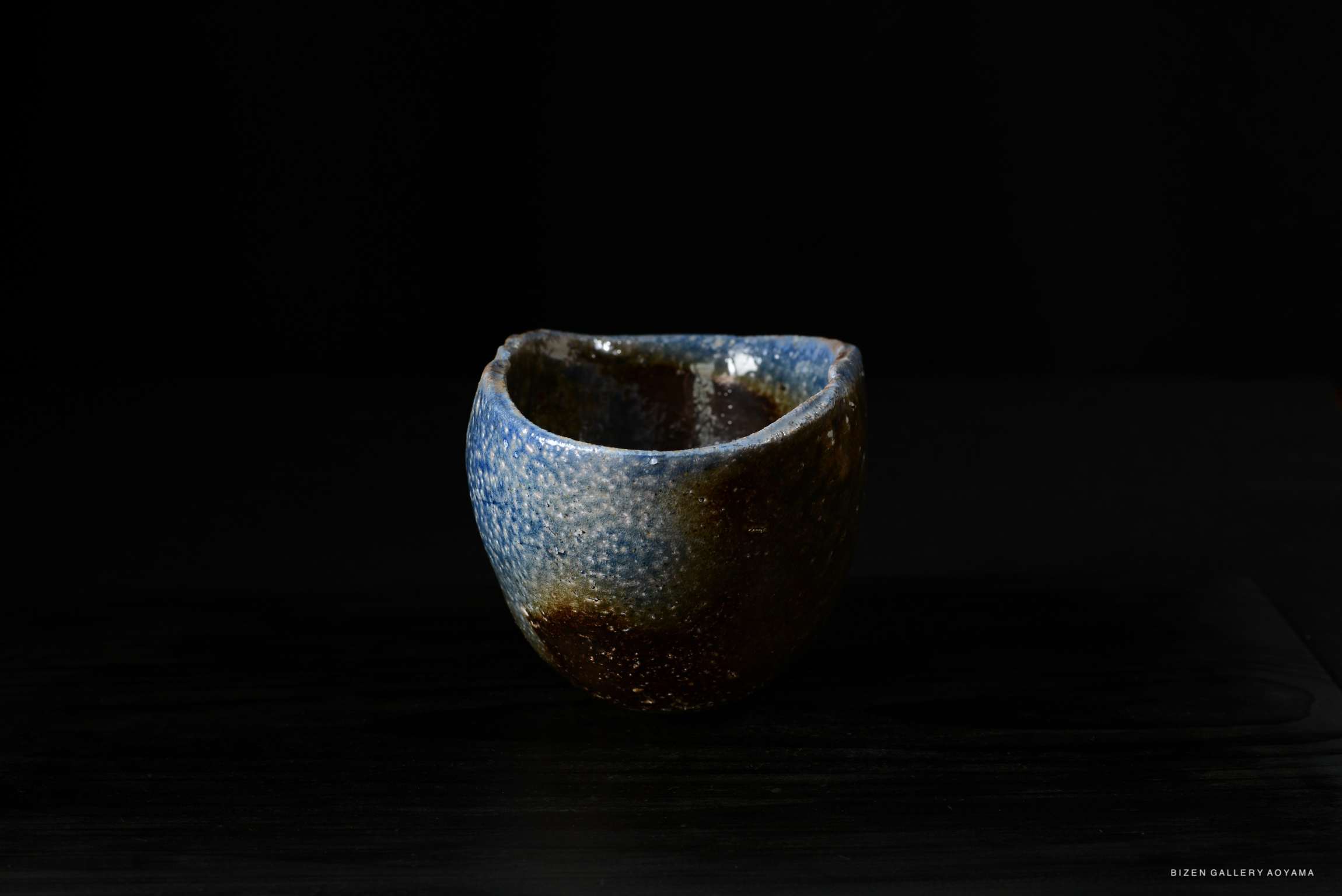 A beautifully crafted ceramic bowl with a blue and brown glaze, resting on a dark surface against a black background.