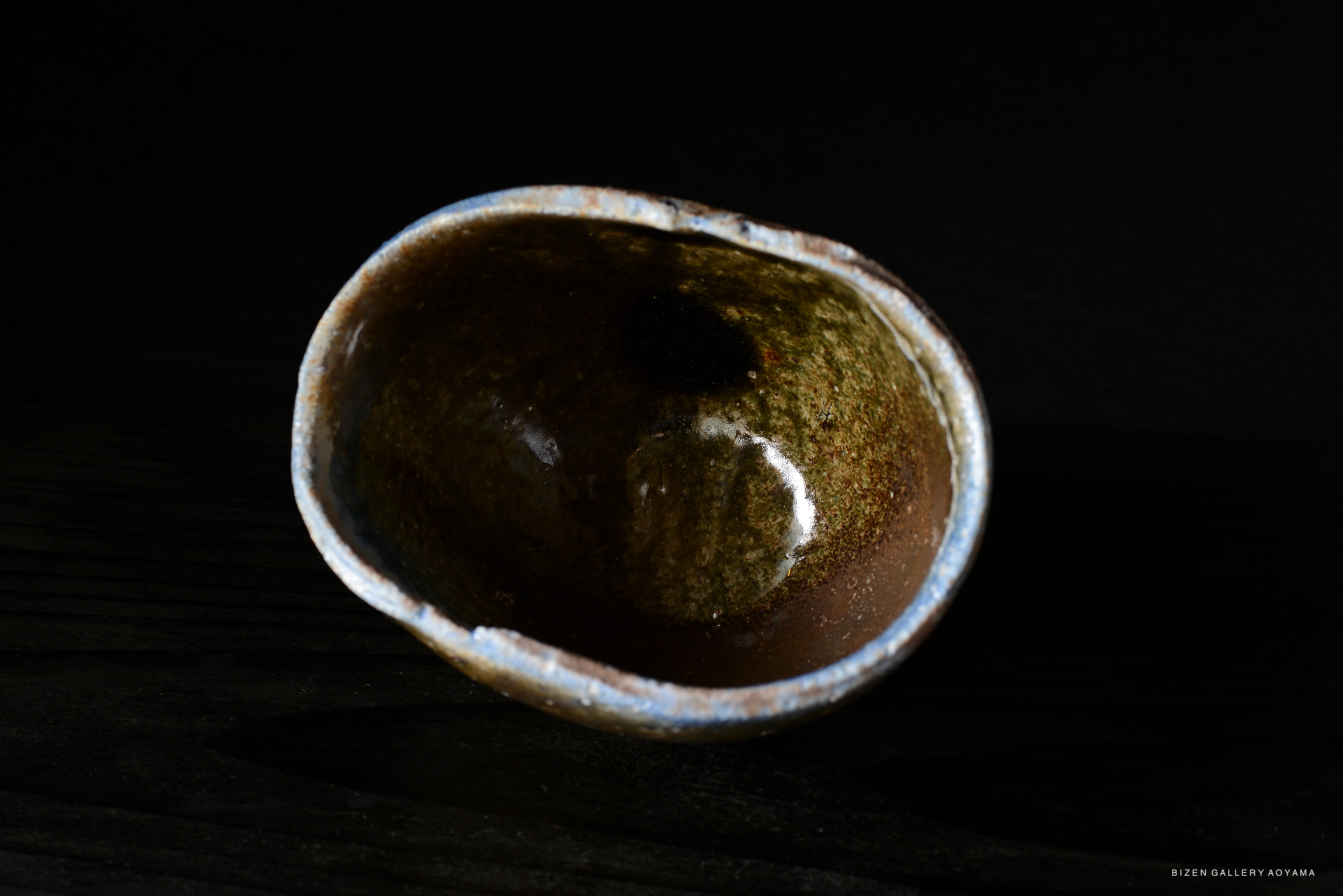 A close-up of a handmade ceramic bowl with a rustic, earthy glaze, set against a dark background.