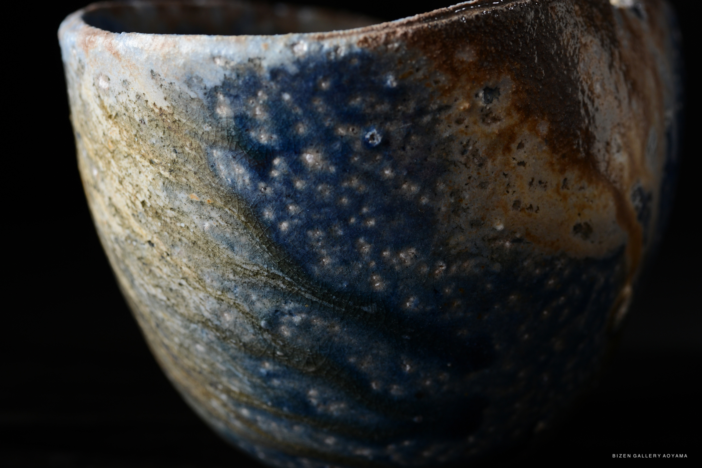 Close-up of a textured ceramic bowl with a blend of blue and earthy tones, showcasing a unique glaze finish.