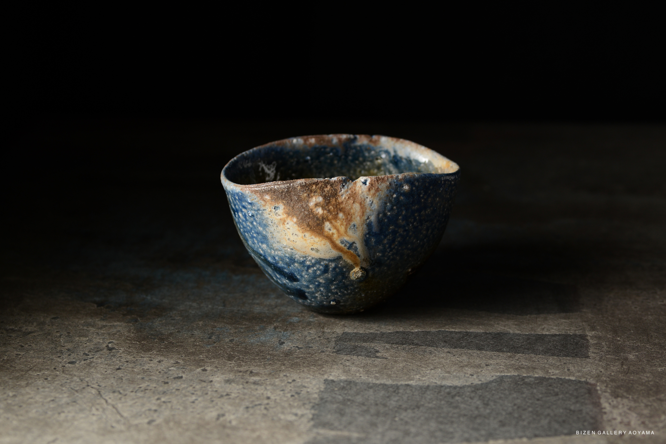 A blue and brown ceramic bowl with a textured surface, displayed against a dark background.